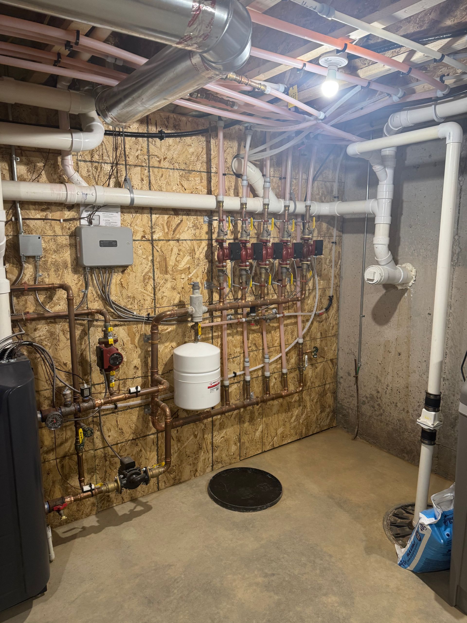 Basement utility room with exposed pipes, valves, a water heater, and concrete floor.