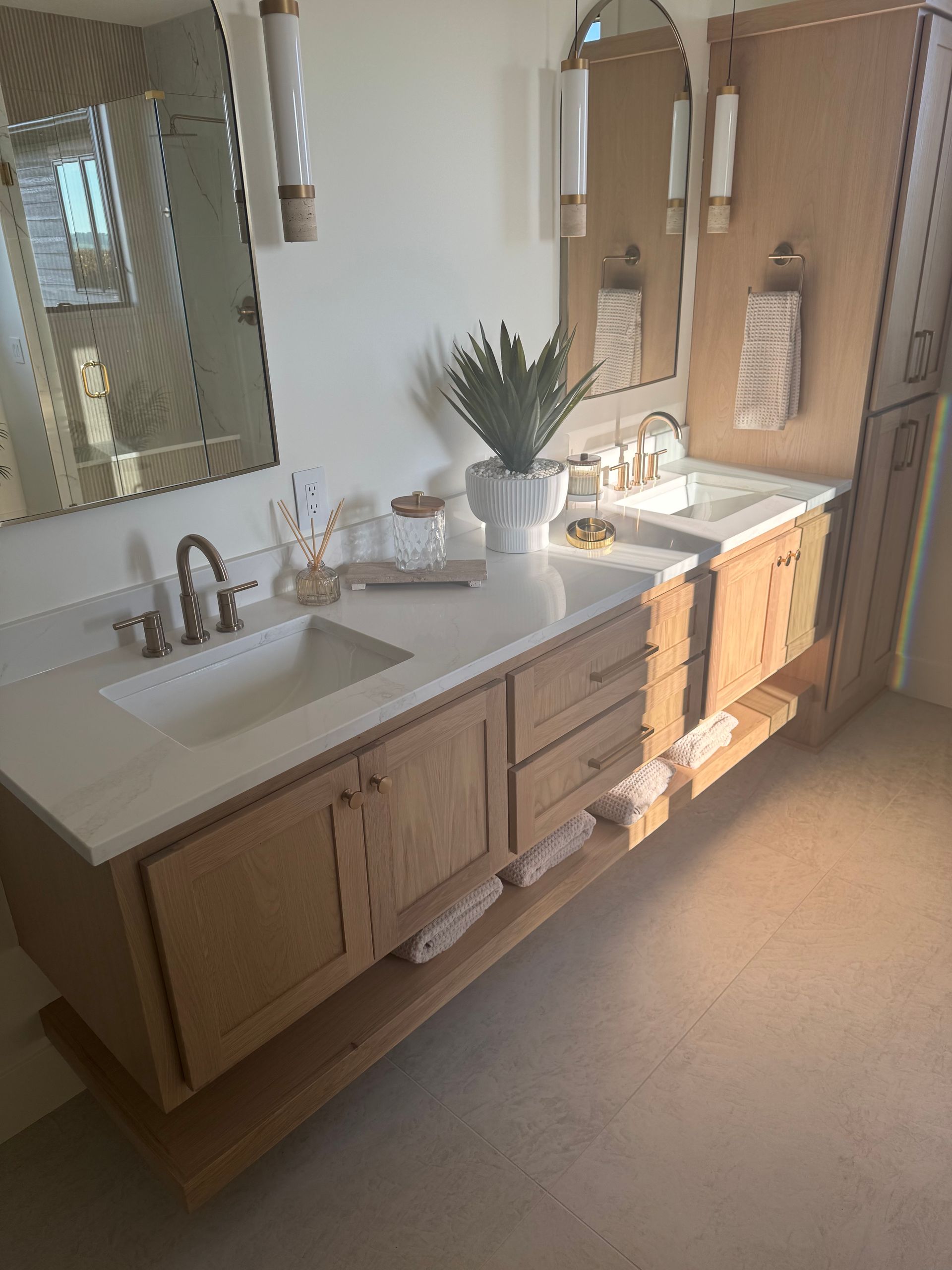 Double-sink bathroom vanity with wood cabinets, large mirror, and a potted plant on the counter.