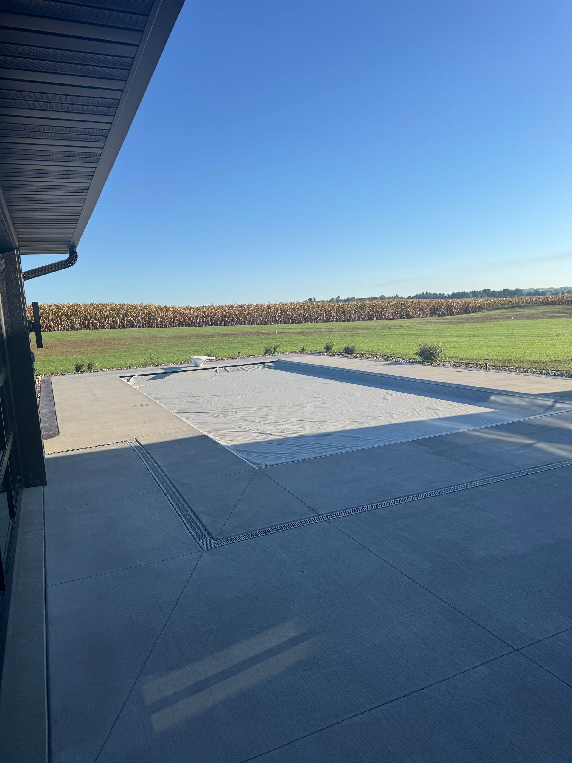 Covered patio overlooking a grassy yard and open field under a clear blue sky
