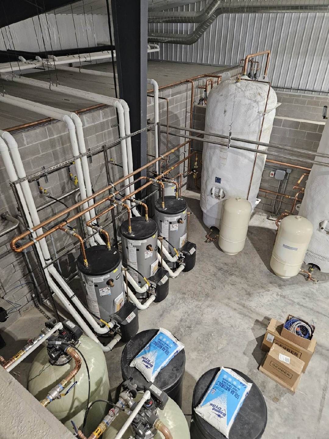 Industrial machinery and tanks in a utility room, with pipes and electrical equipment on the floor and wall.