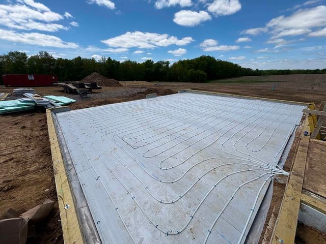 White concrete foundation slab at a construction site under a blue sky, with dirt and trees around it
