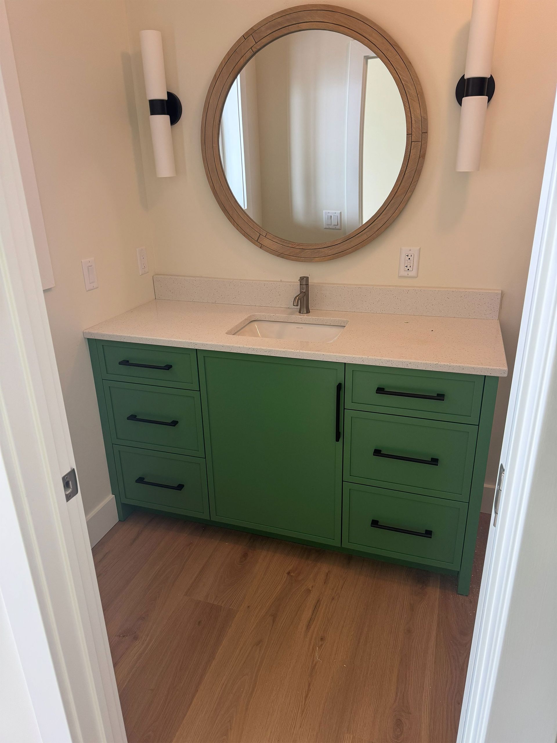 Green vanity with white countertop and round mirror in a bathroom alcove.