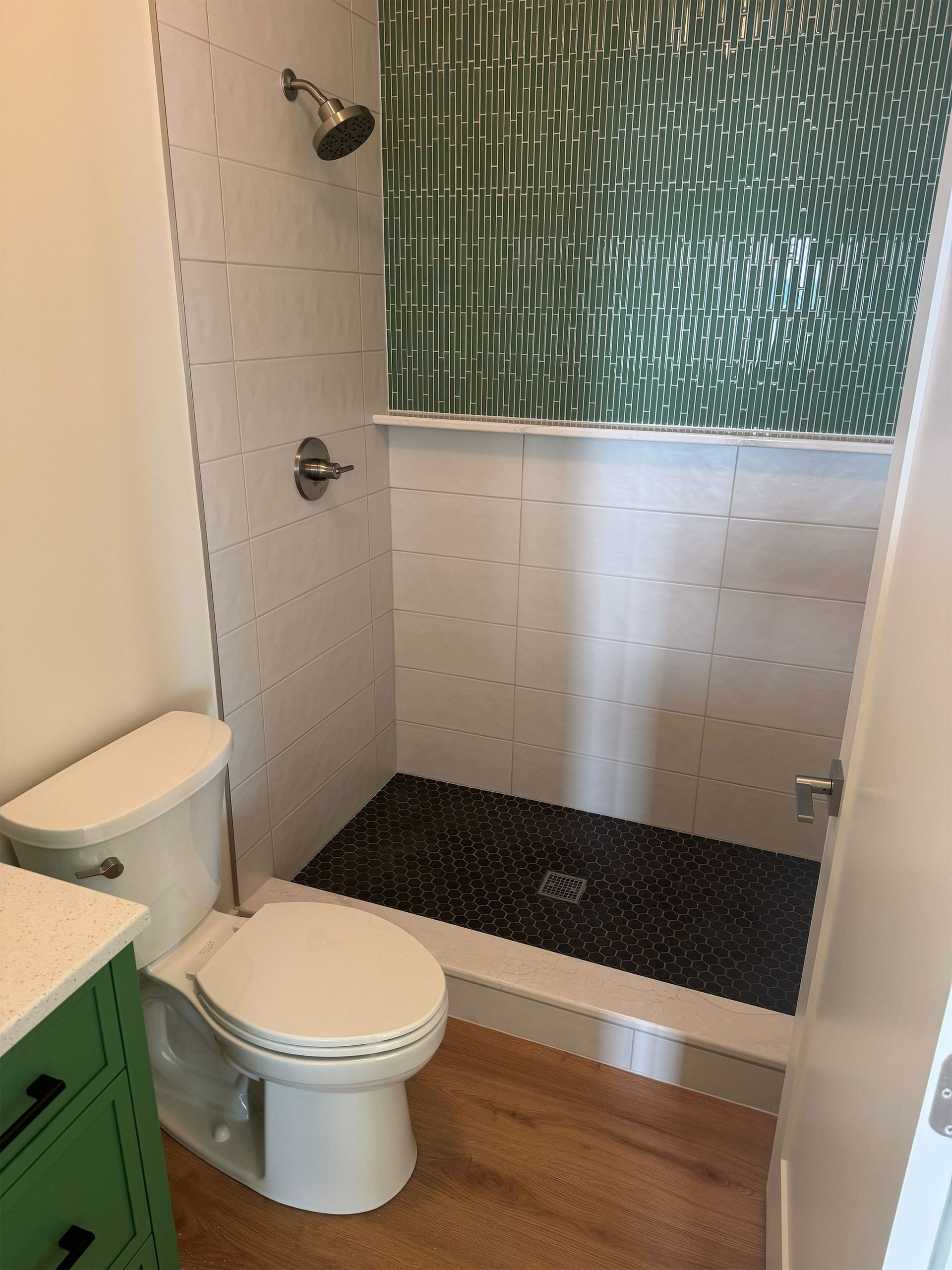 Small bathroom with toilet, green vanity, and shower with glass door and white tile.