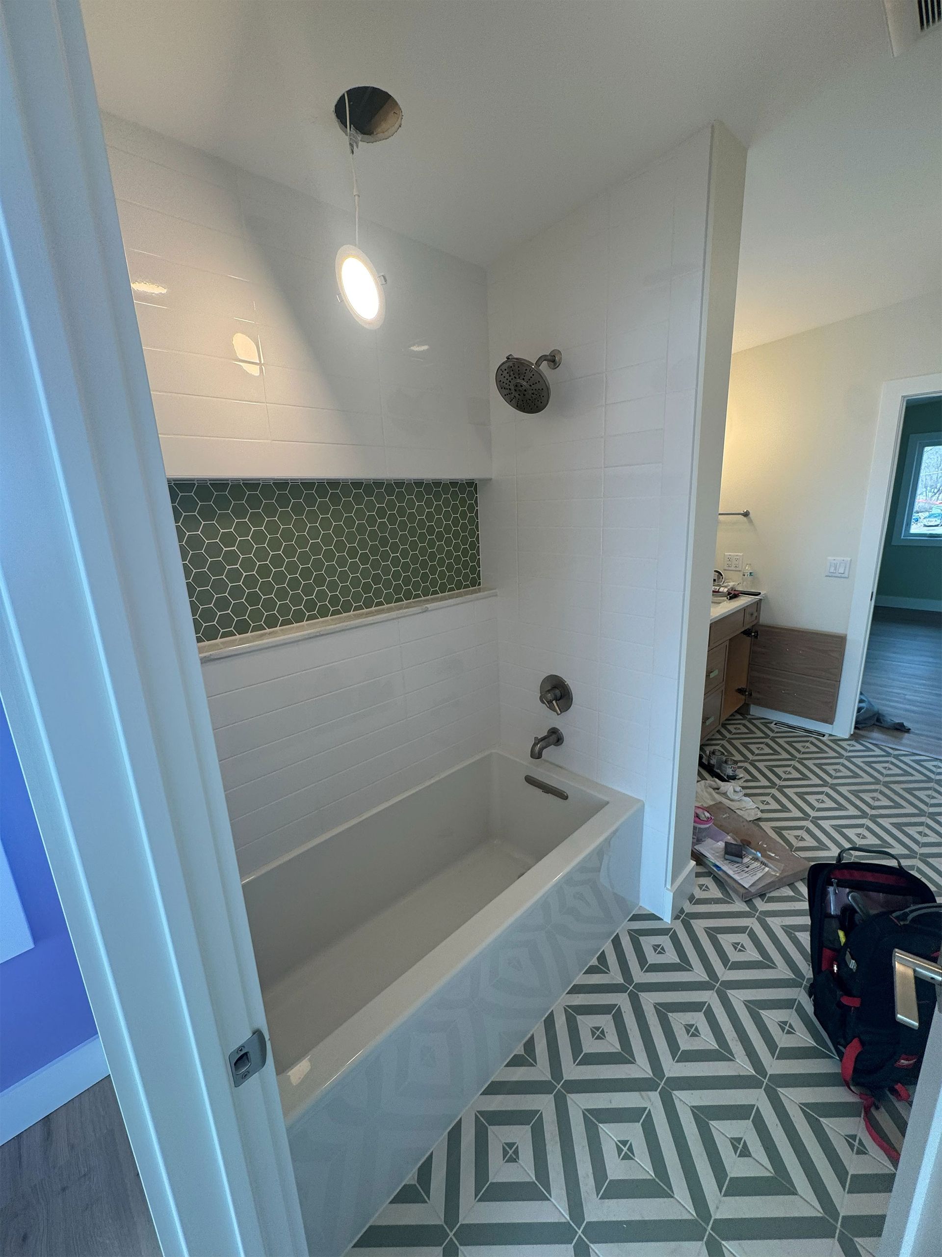 Bathroom with white tub and shower, green tile accent, and patterned floor tiles; doorway visible.