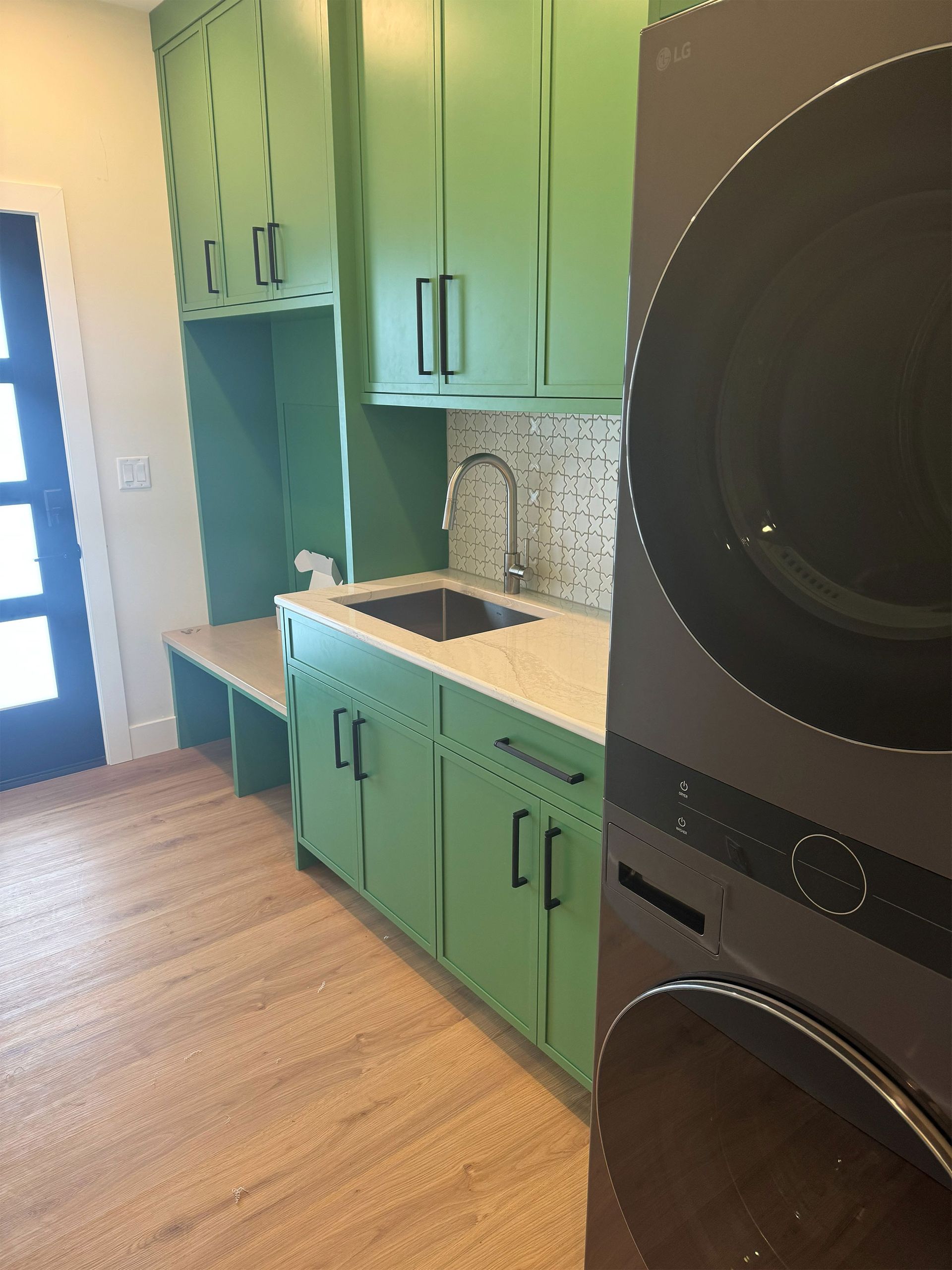 Laundry room with green cabinets, beige countertop, and stacked black washer and dryer.