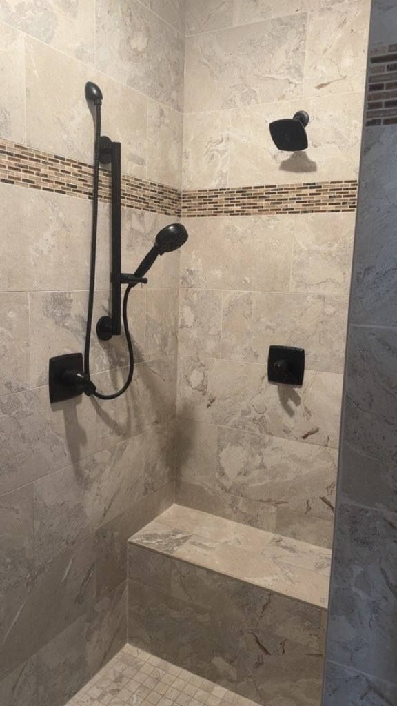 Tiled bathroom shower with handheld sprayer, wall-mounted showerhead, corner shelf, and bench seat.