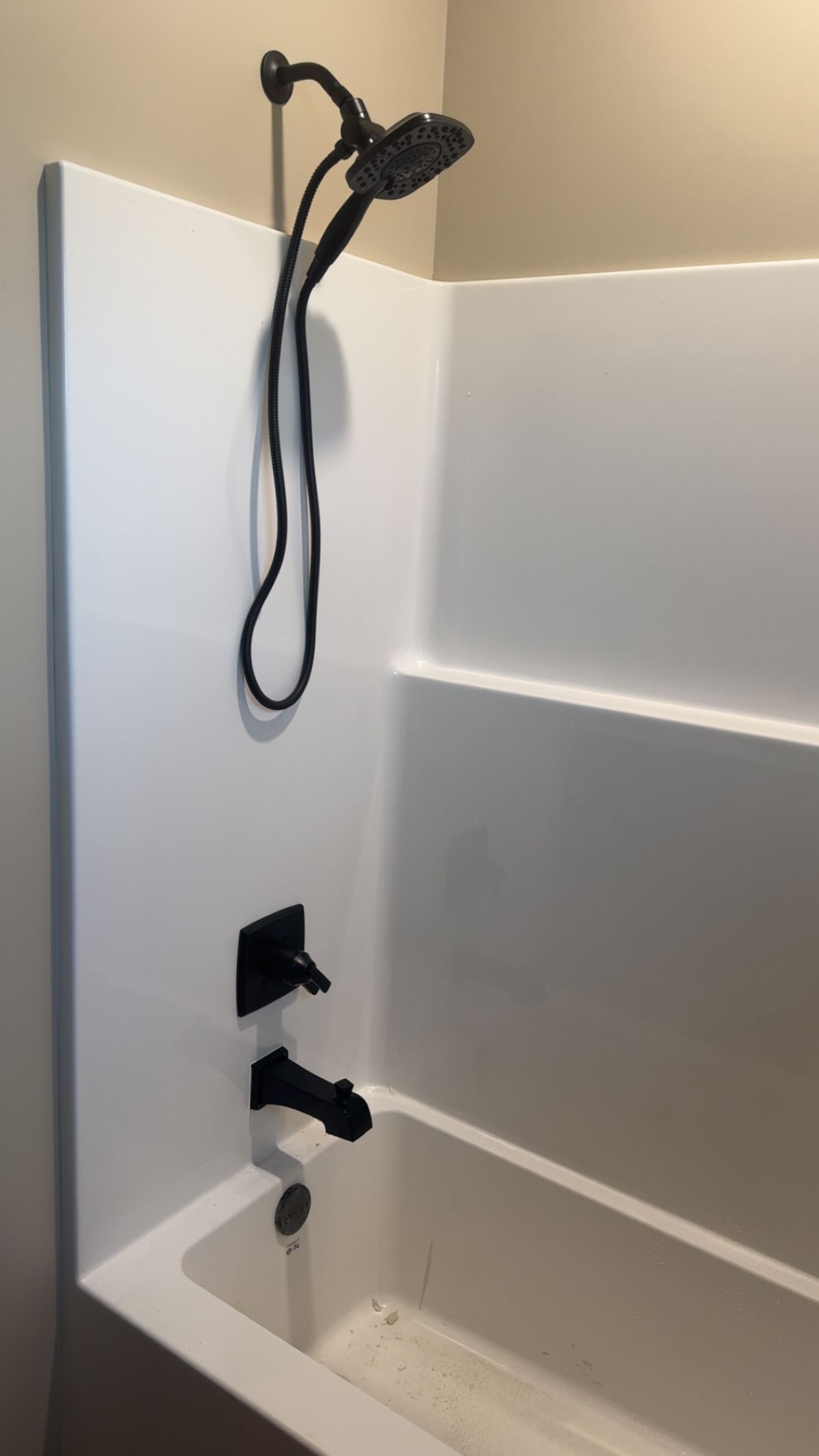 White bathtub with wall-mounted black shower head and faucet in a tiled bathroom