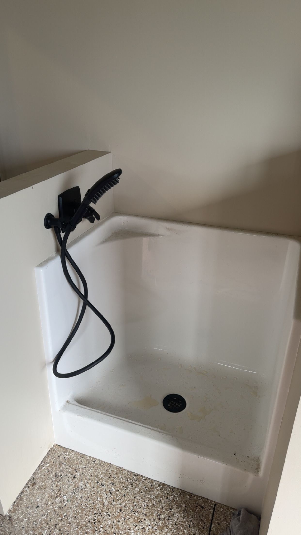 White utility sink with black faucet in a beige corner, on a speckled floor.