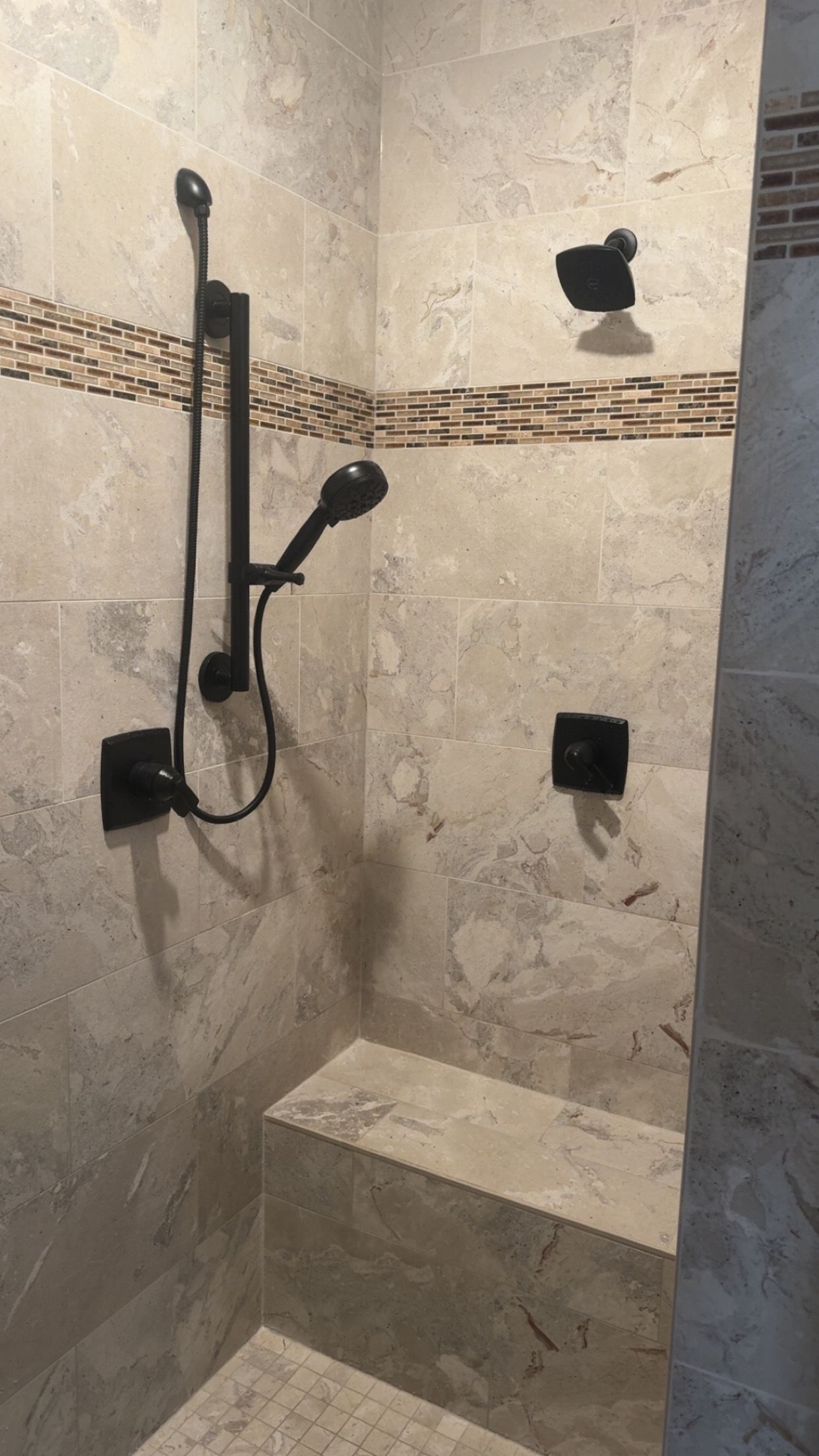 Tiled shower with black handheld showerhead, grab bars, and a built-in bench seat