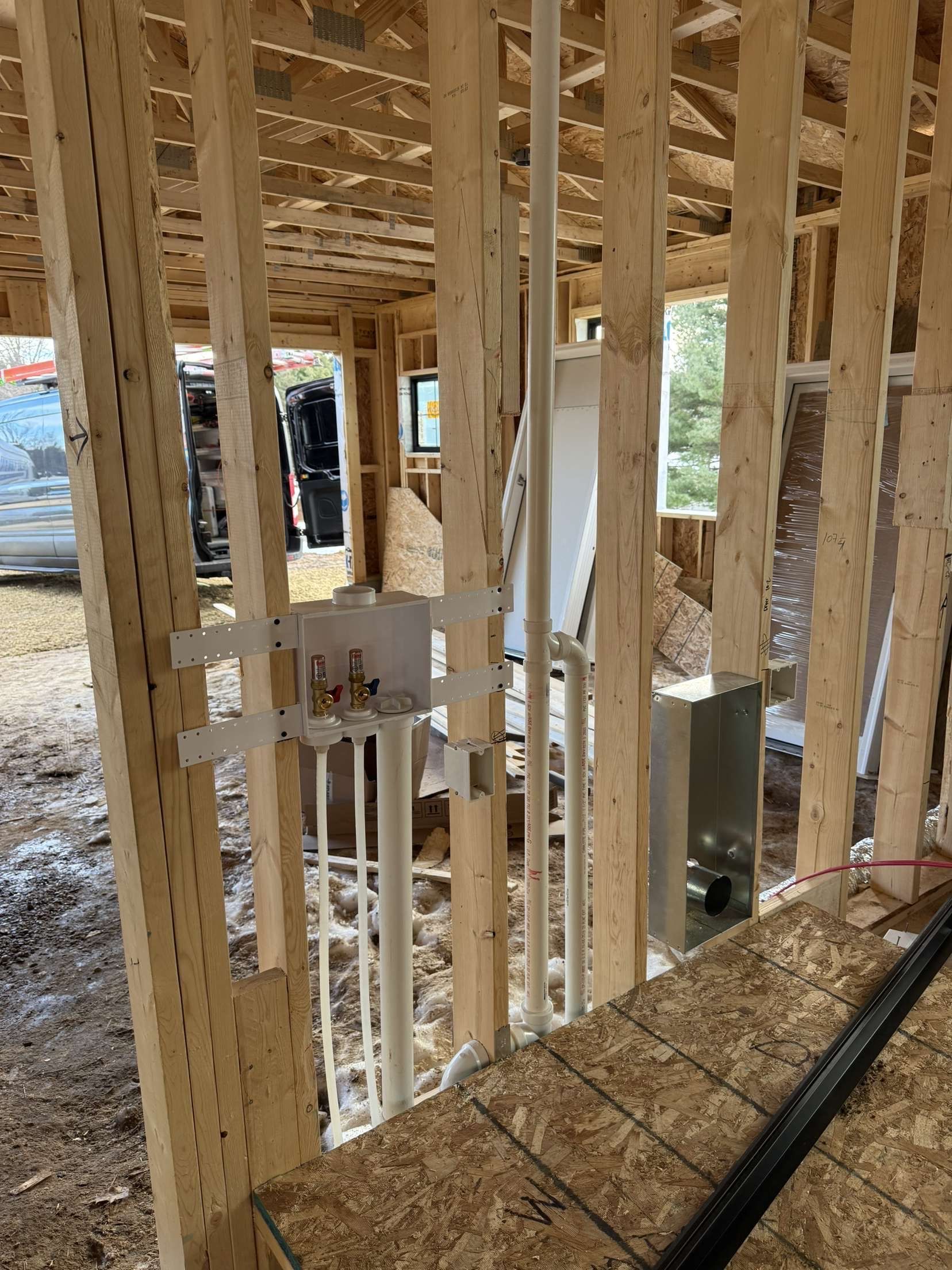 Framed interior of a house under construction with exposed studs and plywood subfloor.