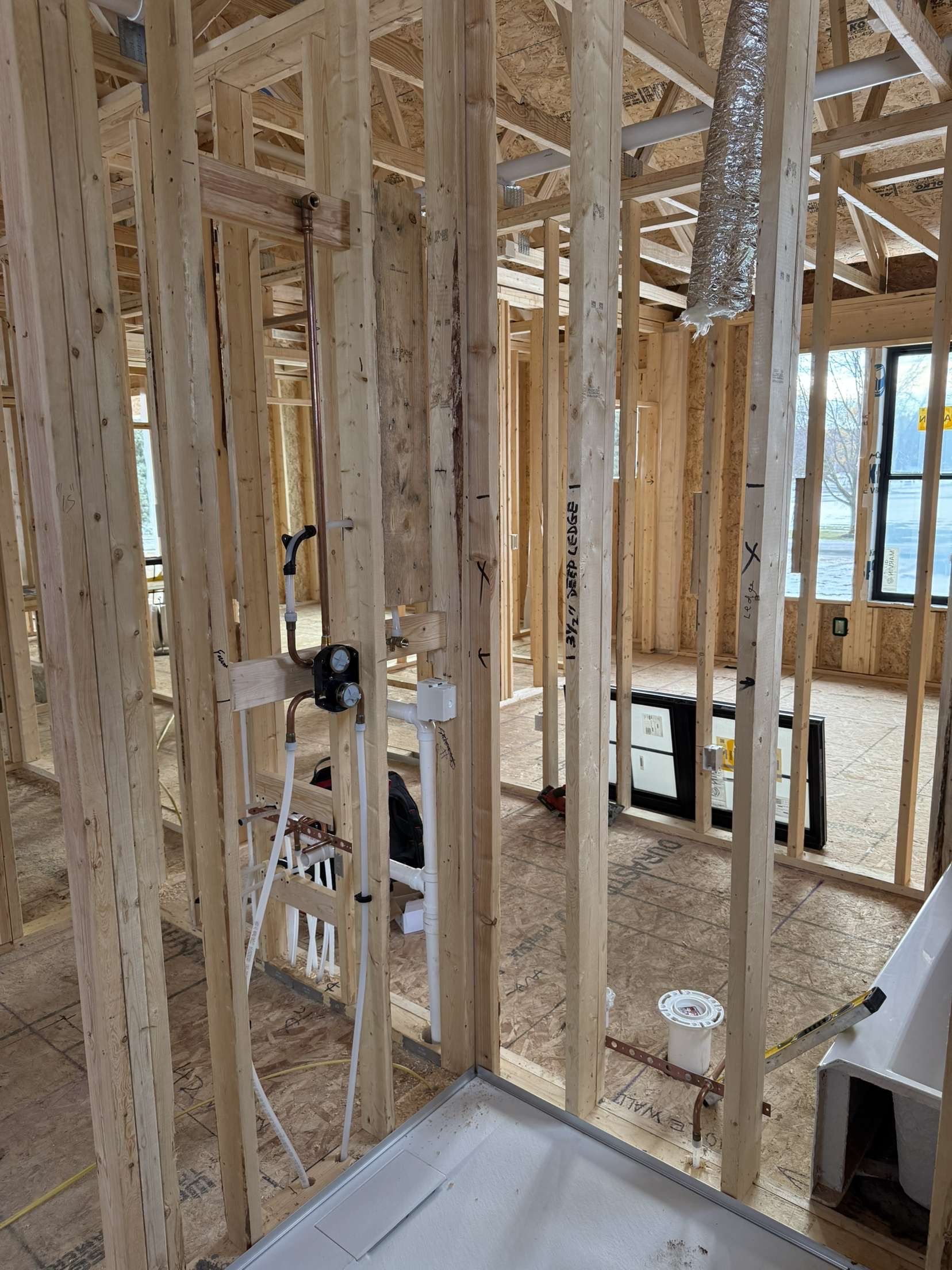 Interior of a house under construction with exposed wood framing, wiring, and a window in the background