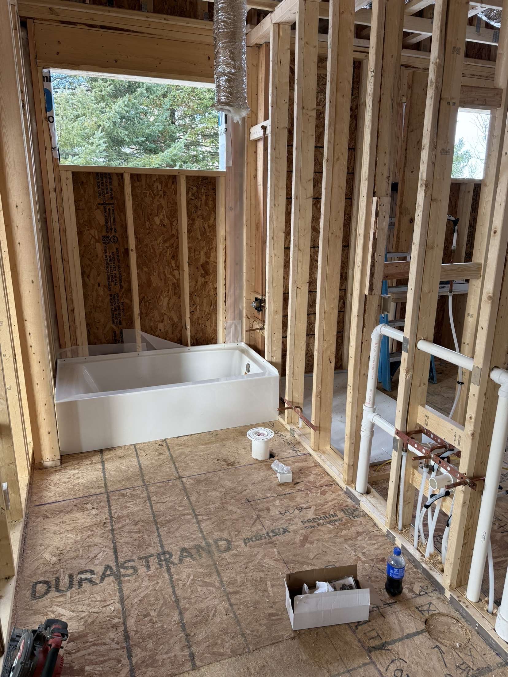 Unfinished bathroom framing with bathtub alcove, exposed studs, and subfloor under construction.