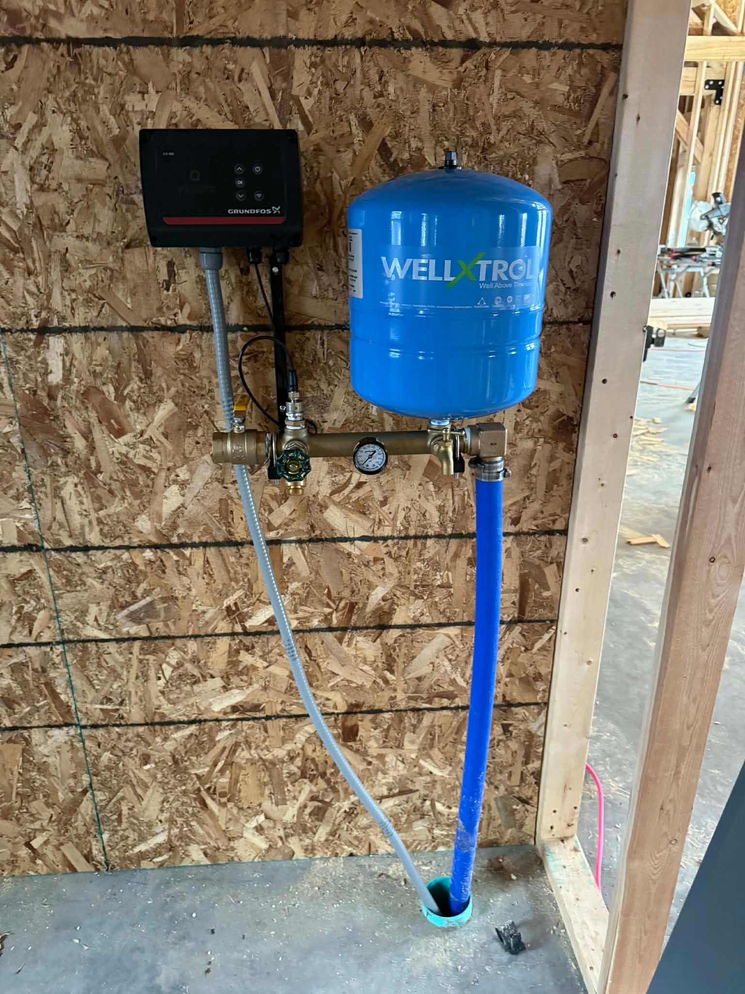 Blue well pressure tank and control box mounted on an OSB wall in a utility space