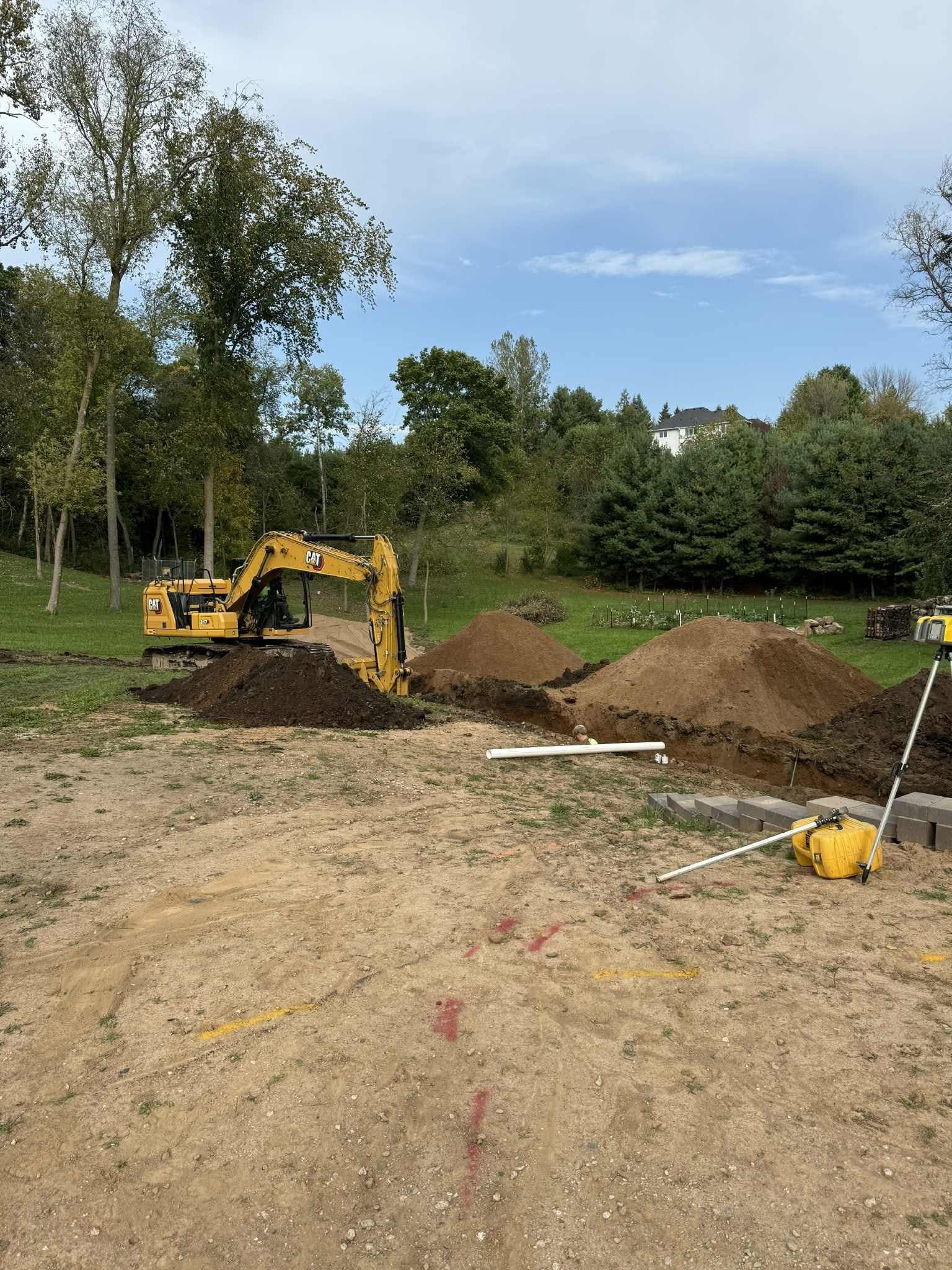Yellow excavator digging dirt piles on a grassy lot under a blue sky