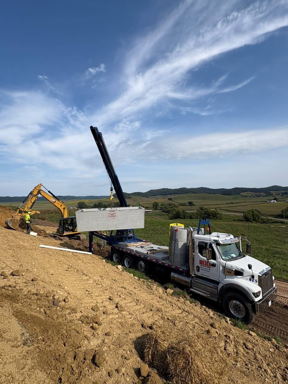 Heavy equipment lifting a concrete slab at a construction site on a hillside under a blue sky