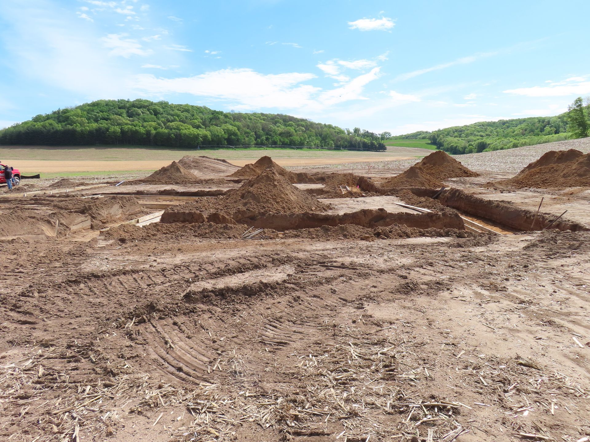 Dirt excavation site with piles of earth and muddy tracks under a cloudy sky