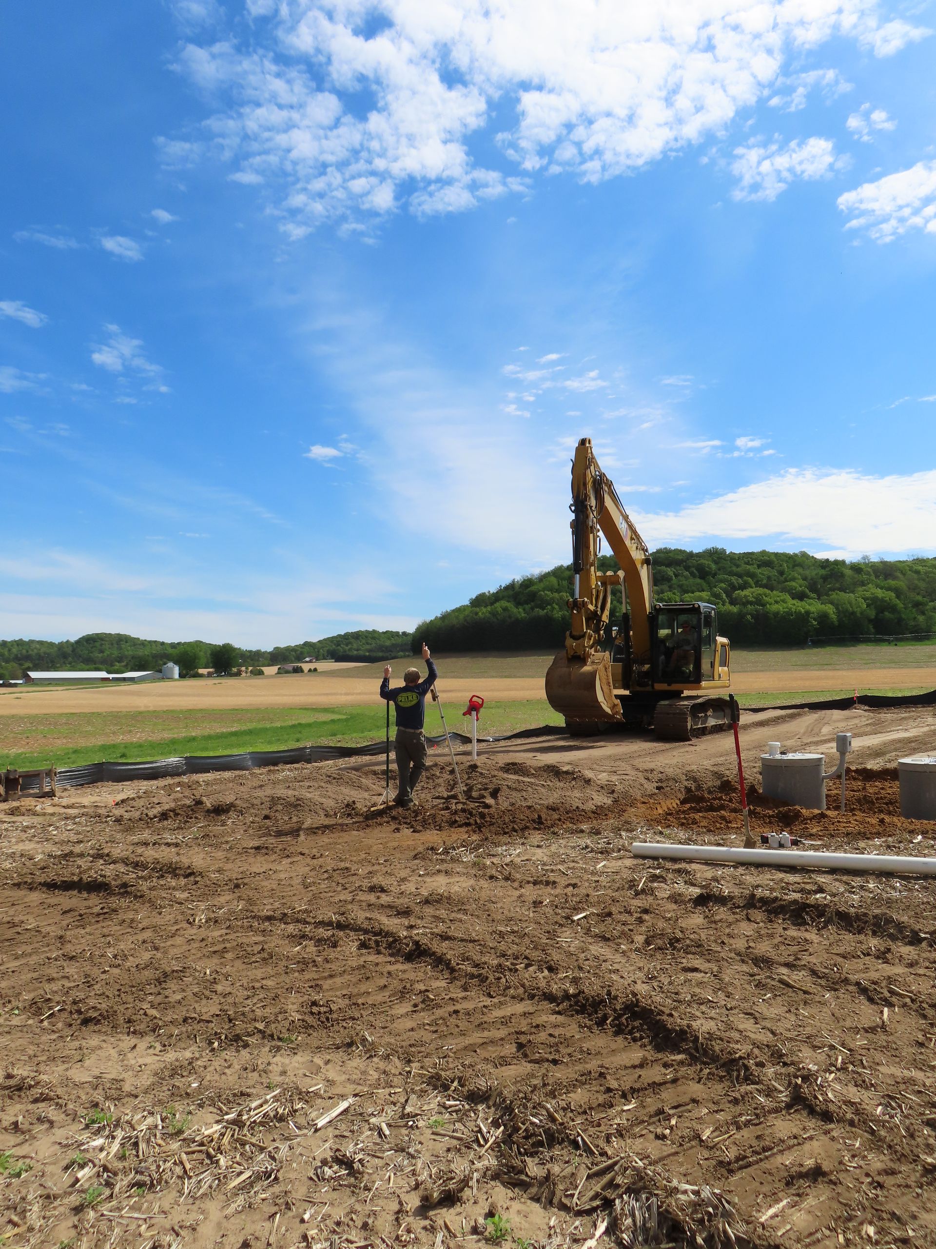 Construction site with excavator and worker on dirt field under a blue sky