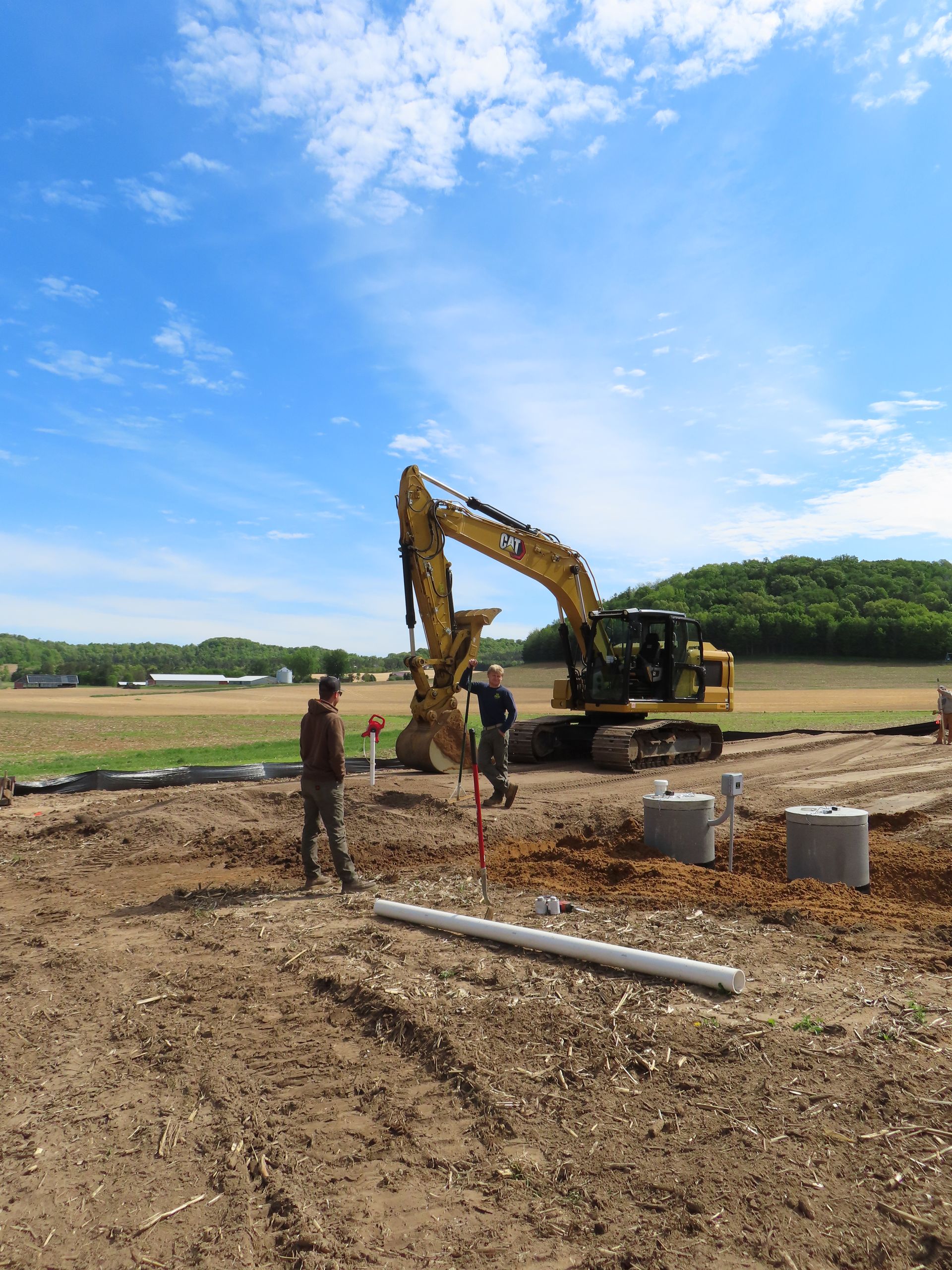 Workers beside excavator at a dirt construction site under a bright blue sky