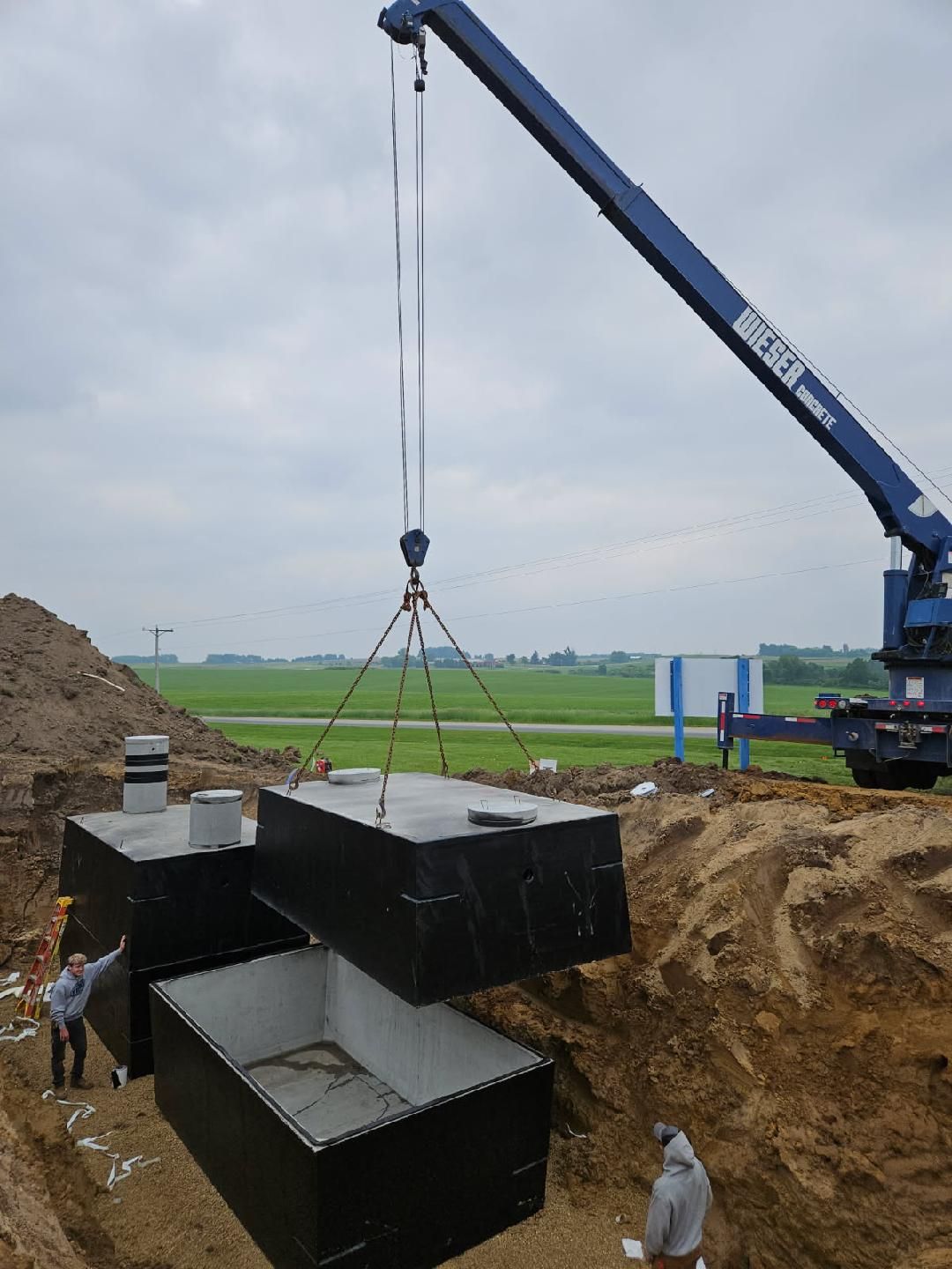 Crane lifting large concrete culvert sections at a construction site beside an excavated trench