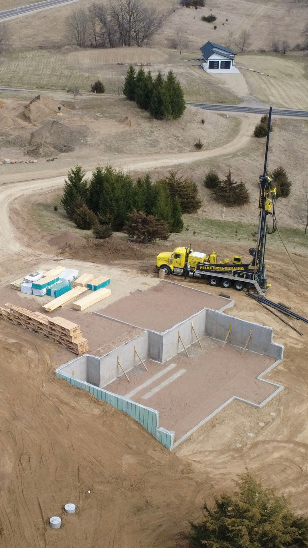 Aerial view of a house foundation under construction with a yellow drilling rig and dirt roads nearby