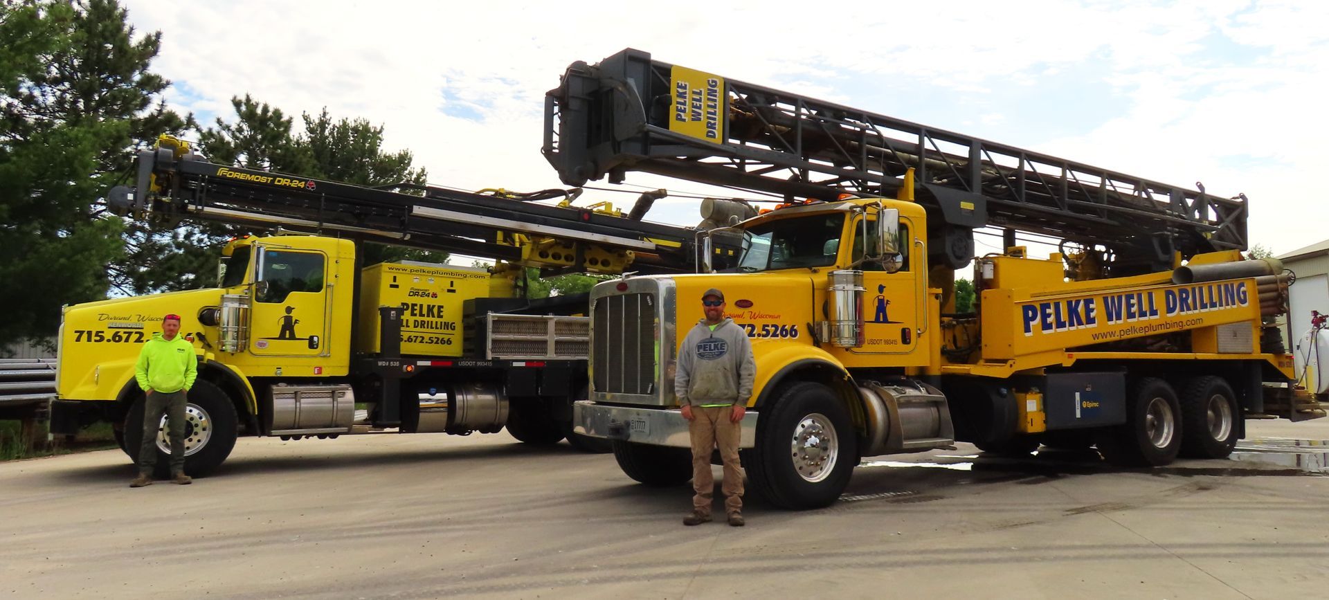 Yellow crane truck with extended boom and a worker standing in front on a road.