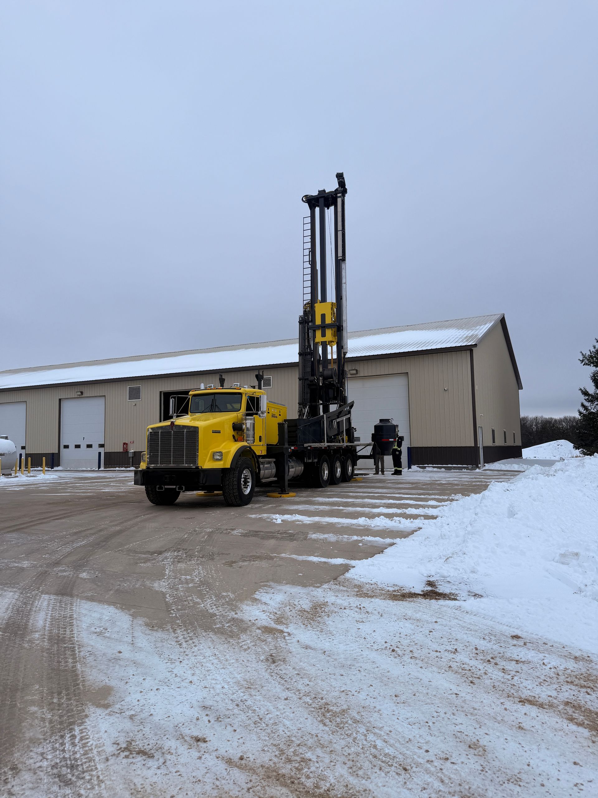 Yellow forklift loading a white metal building in a snowy lot, with one worker nearby.
