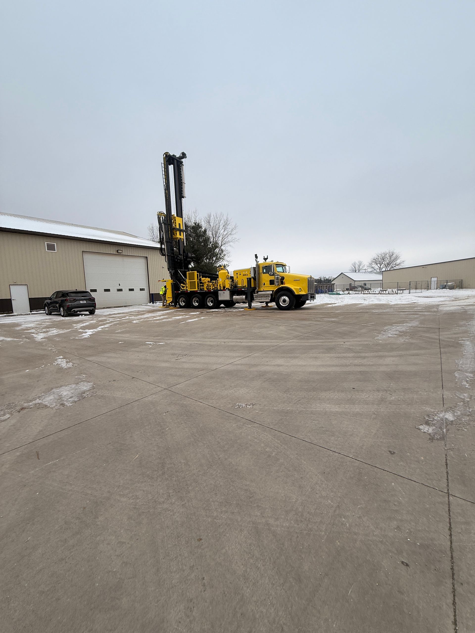 Yellow forklift lifting a black pallet in a snowy industrial yard beside a warehouse