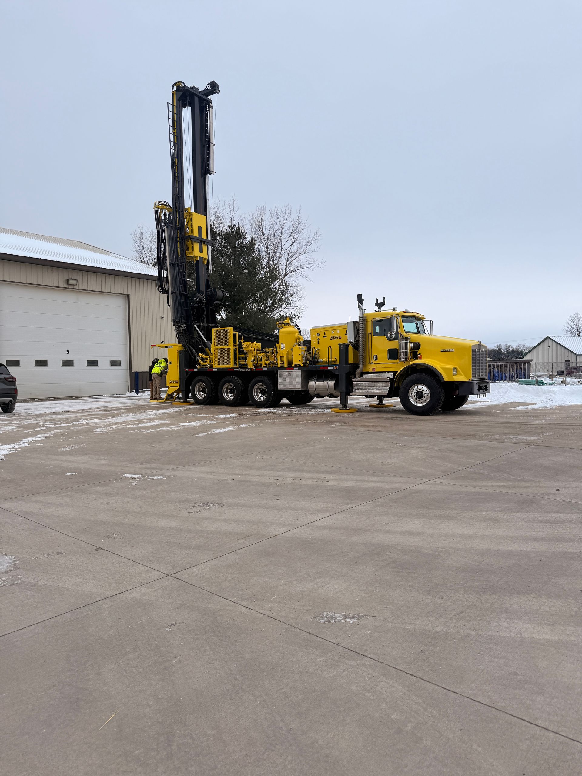 Yellow drilling rig truck parked outside a warehouse on a snowy lot