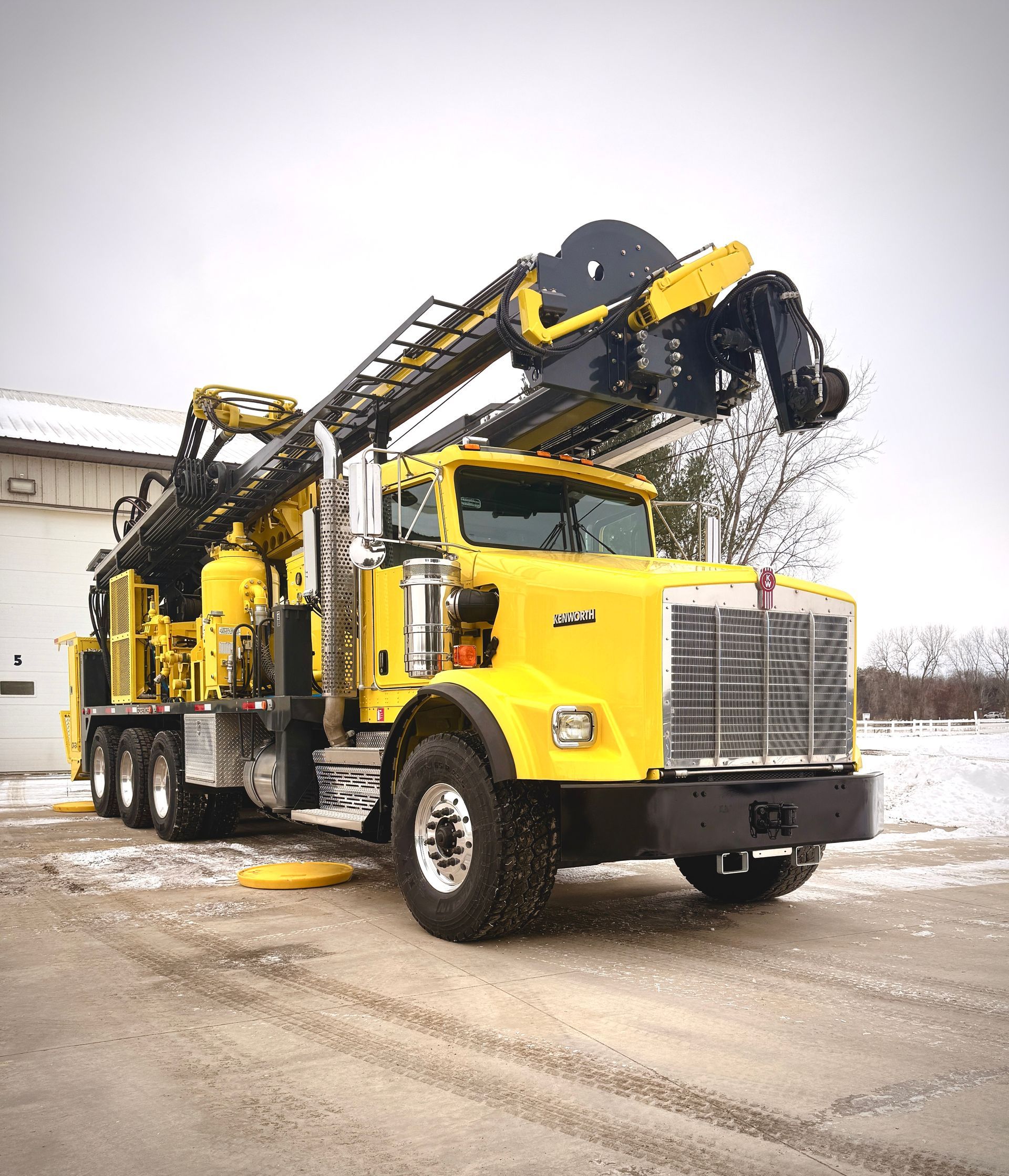 Yellow crane truck with folded boom parked on a snowy industrial lot
