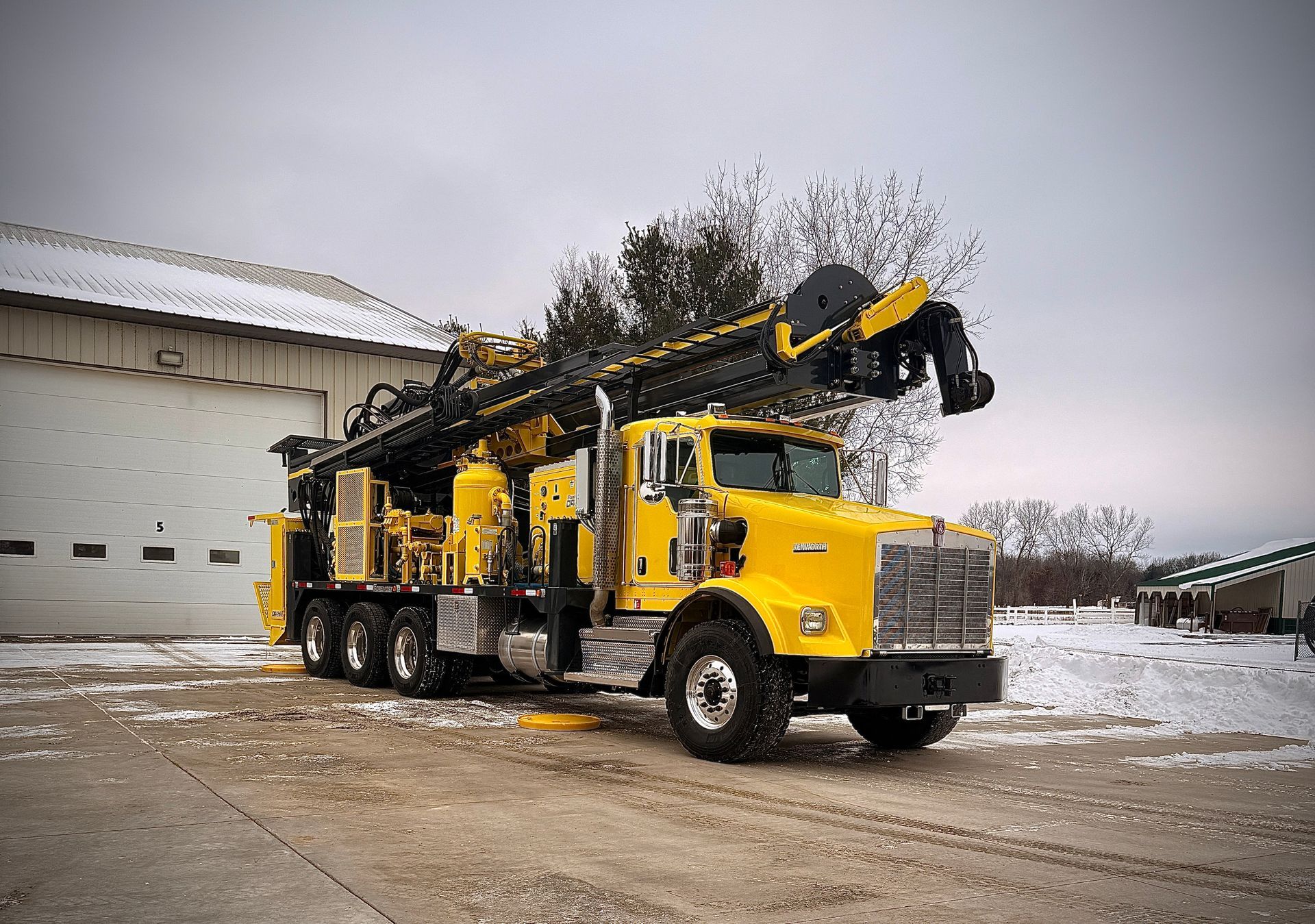 Yellow drilling rig truck parked outside an industrial building on a snowy day