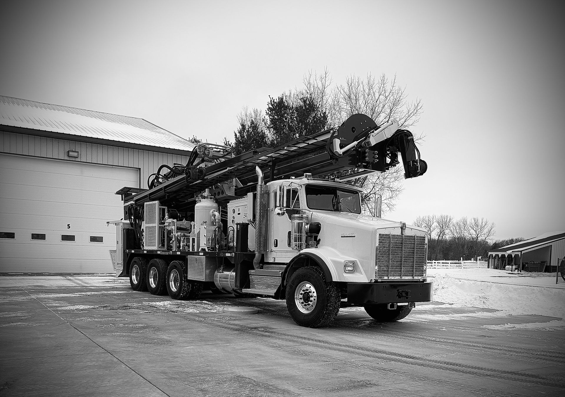 White utility truck with mounted boom lift parked outside a warehouse in a snowy lot