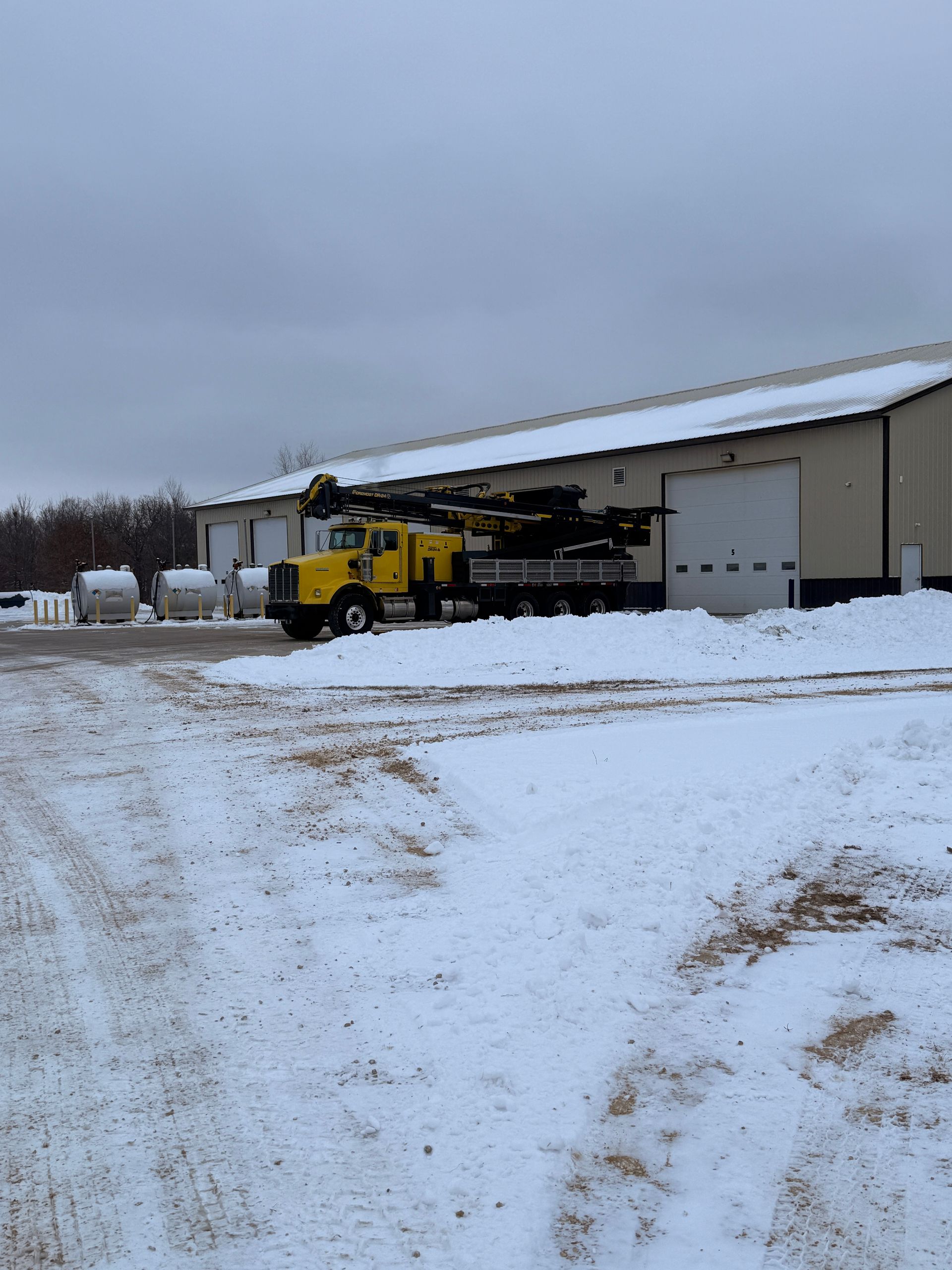 Yellow utility truck parked outside a snowy warehouse under a gray sky