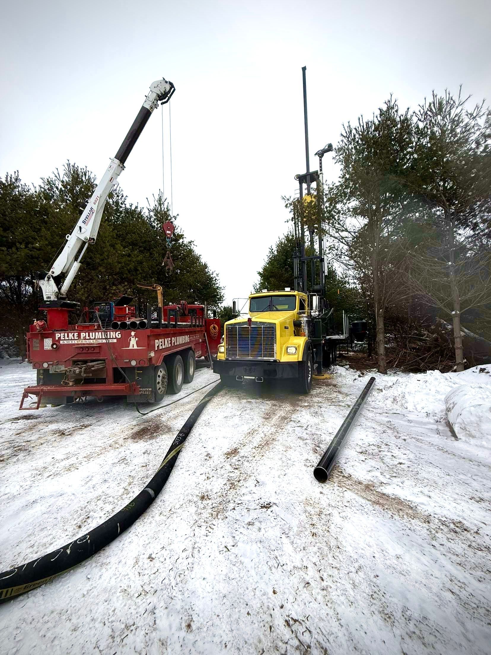 Fire trucks on a snowy road near trees, one with an extended ladder and another with a raised mast.