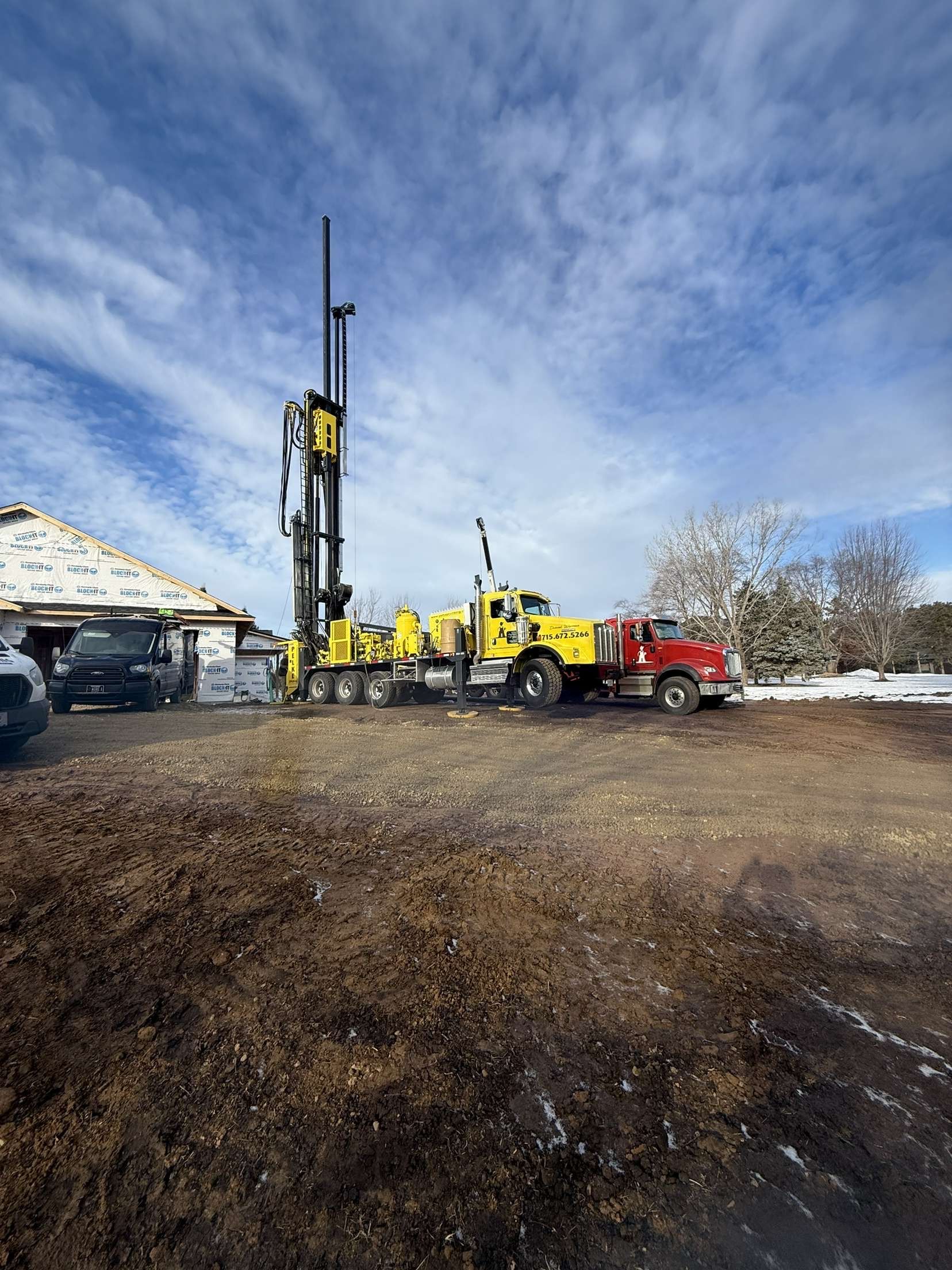 Yellow and red drilling rig on a snowy construction site under a cloudy sky