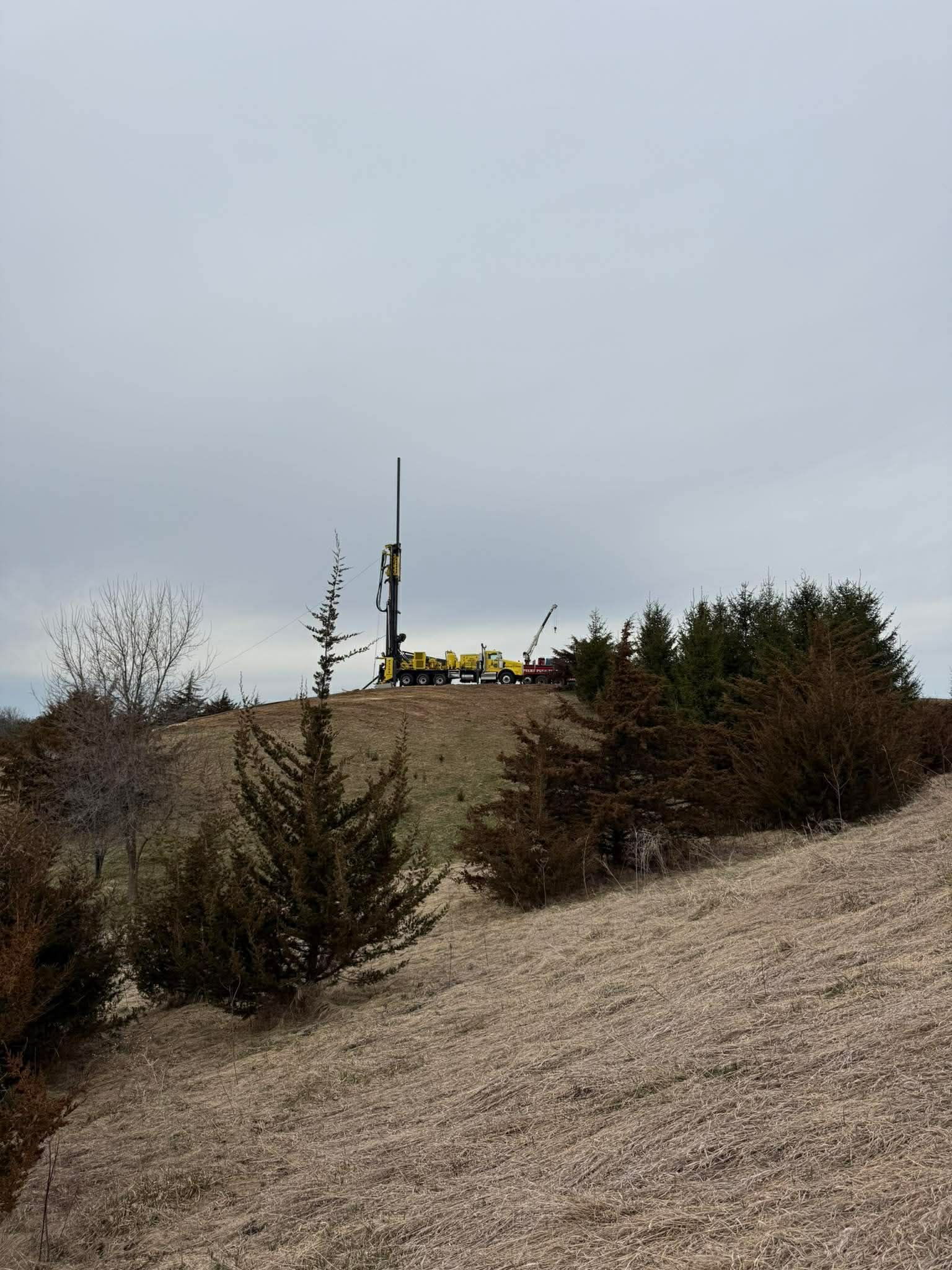 Sparse shrubs on a dry hillside with a small structure and utility pole under an overcast sky
