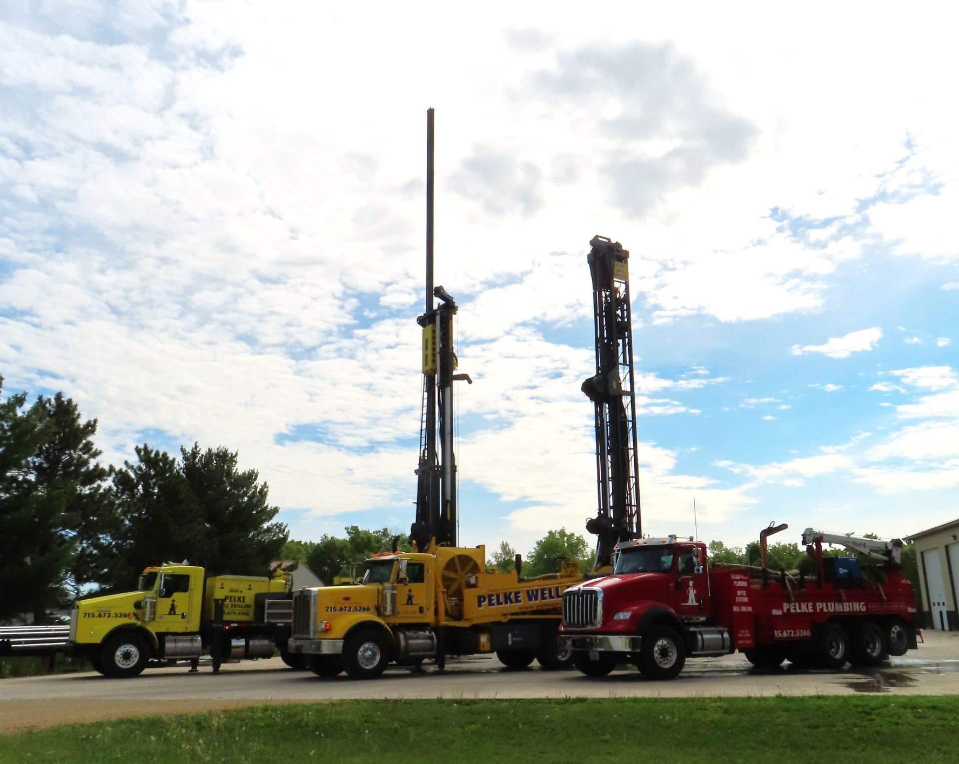 Yellow and red trucks with tall drilling rigs parked on grass under a cloudy sky