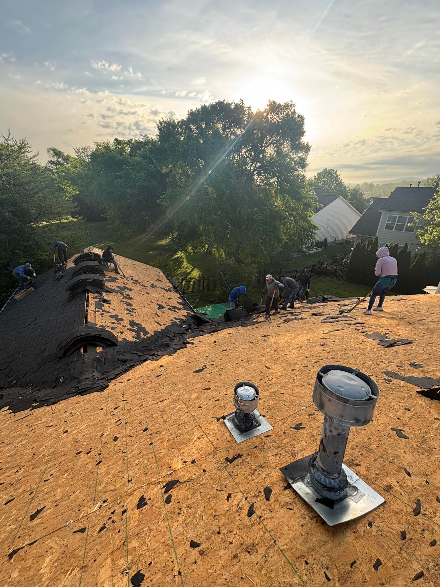 Roofers working on a residential roof under a bright sky.