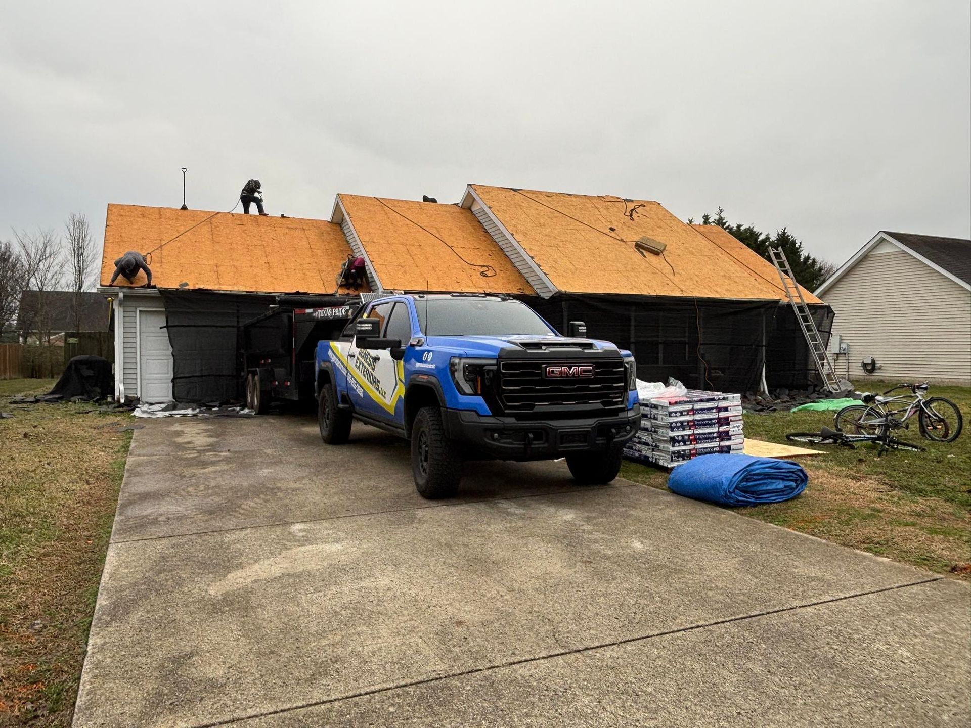 Roofers working on a house with a blue GMC truck parked in the driveway.