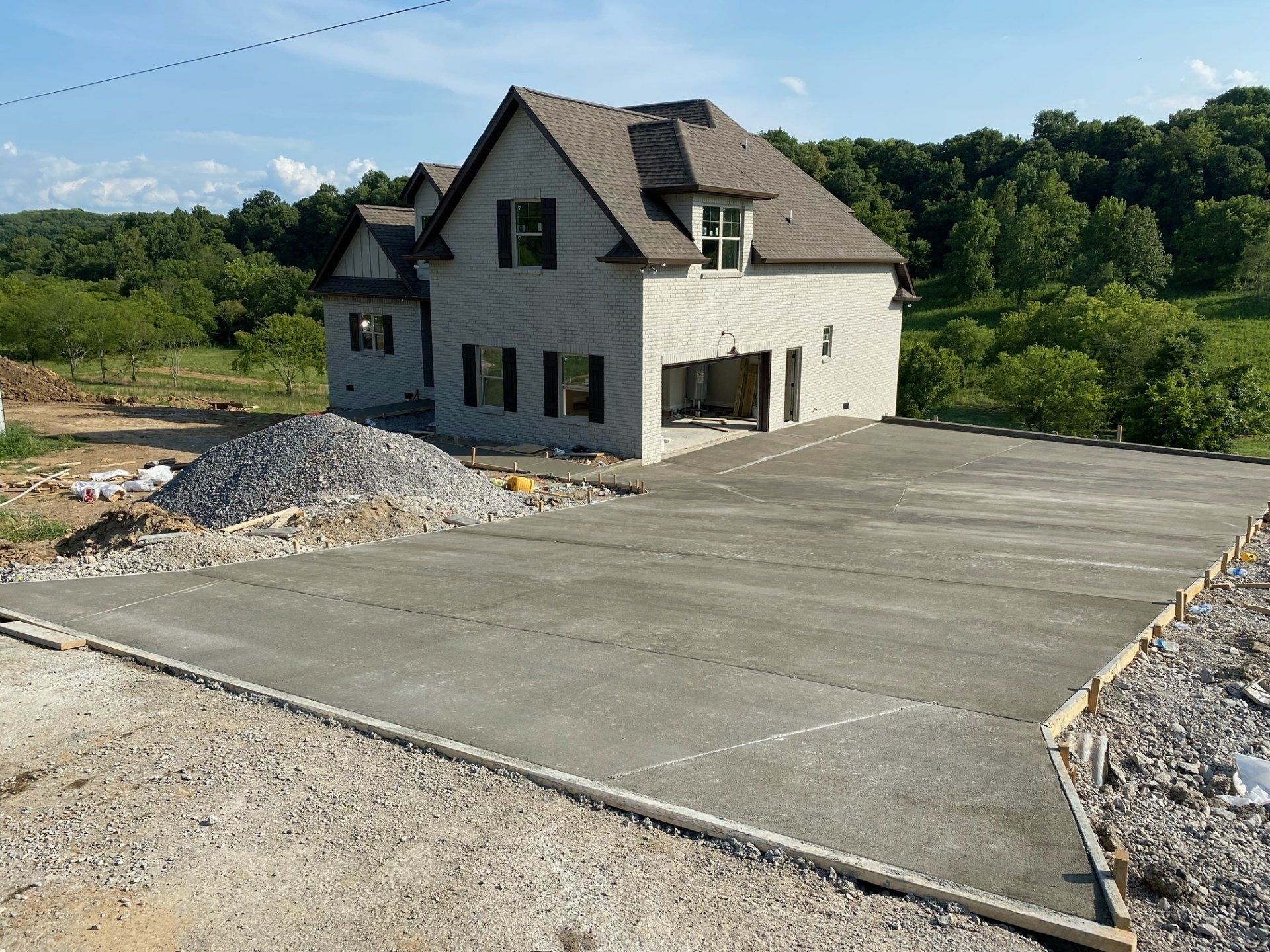 New concrete driveway in front of a light-colored house with a brown roof, under construction on a sunny day.