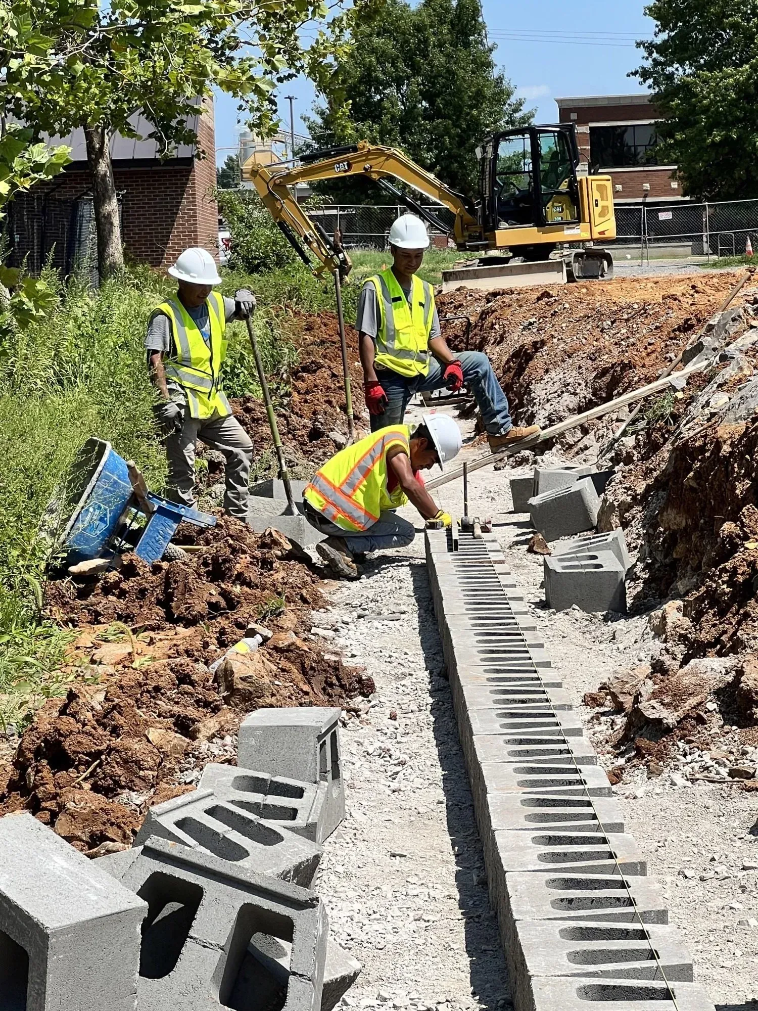 Construction workers building a retaining wall with cinder blocks and equipment.