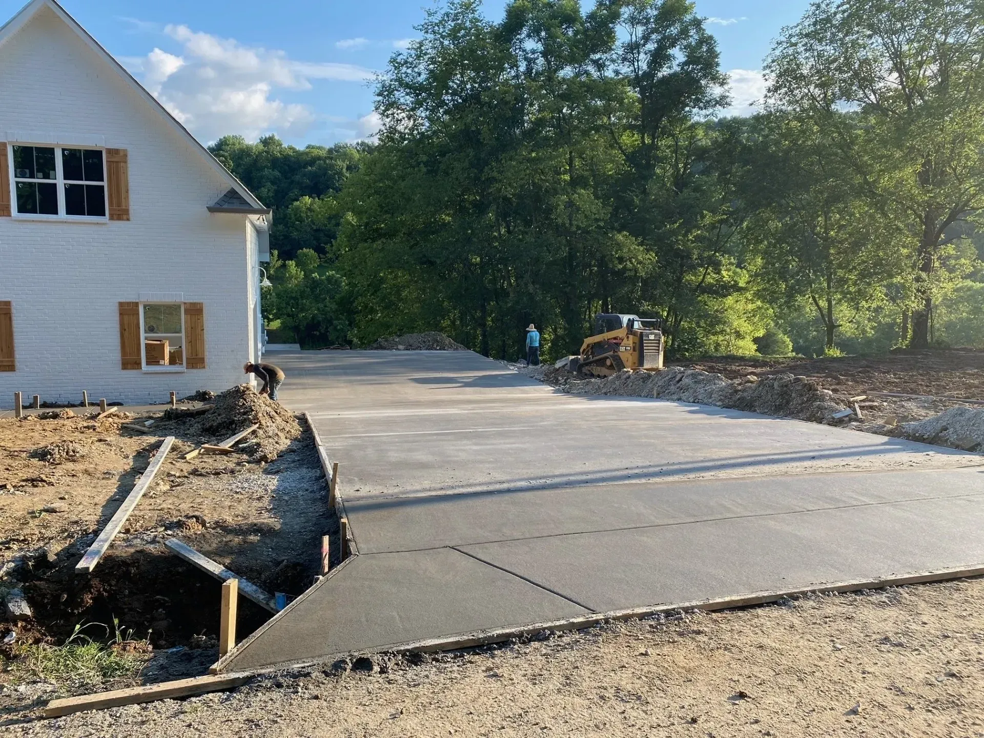 Newly poured concrete driveway at a house under construction; a bulldozer and trees are in the background.