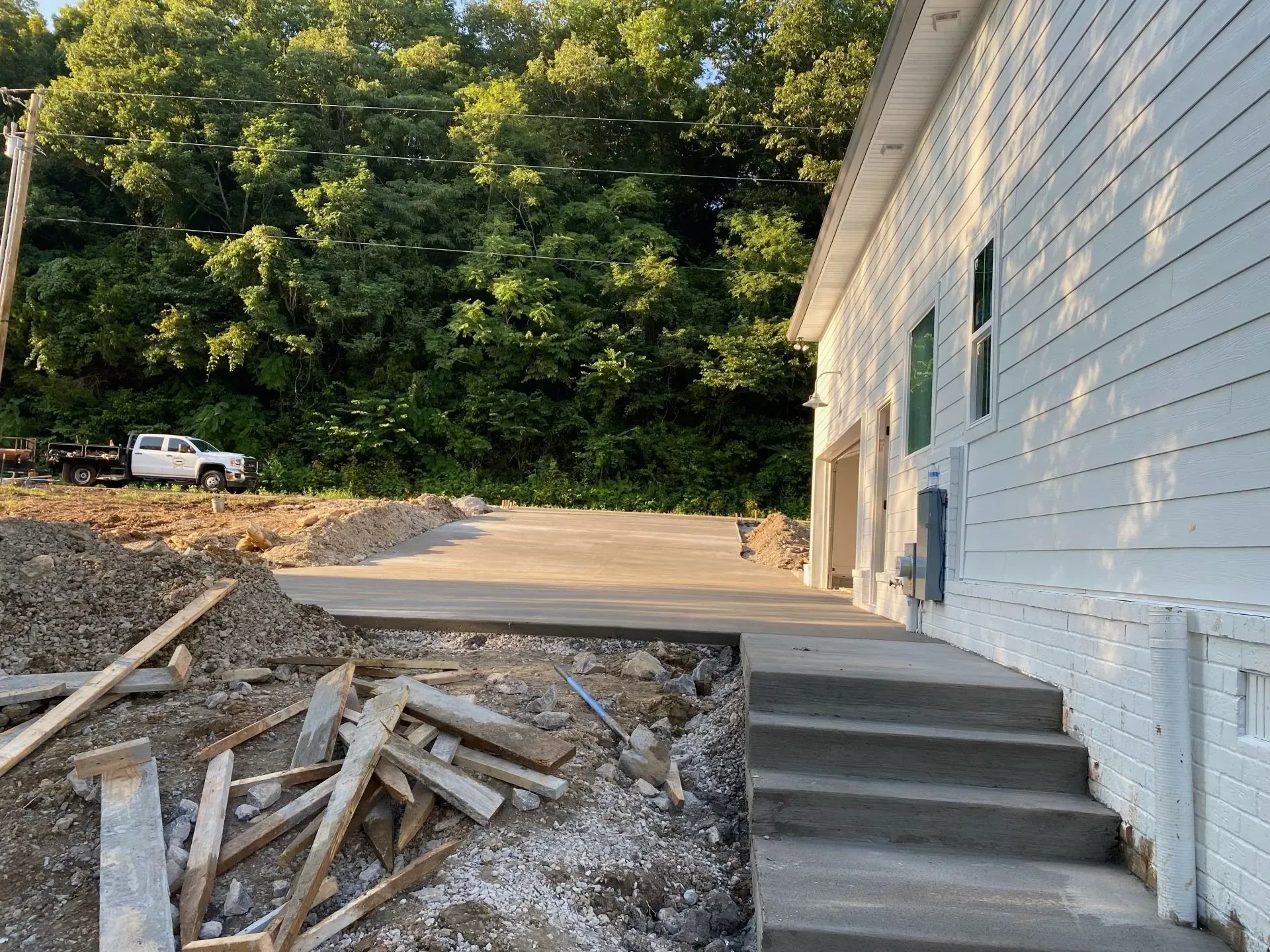 Newly poured concrete steps and pad next to a building. Construction materials are scattered. Trees in the background.