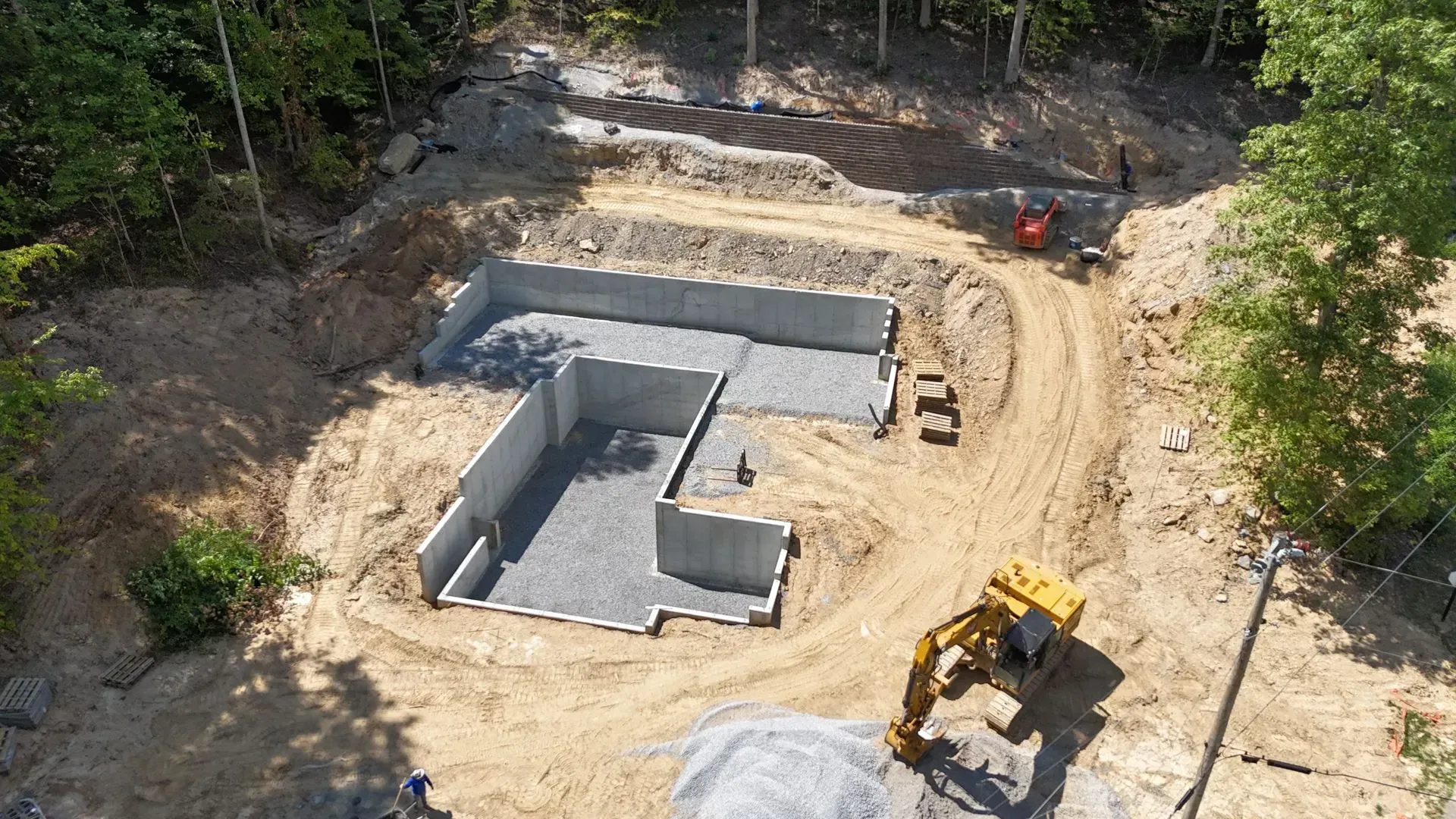 Construction site with concrete foundation walls, earthworks, and machinery.