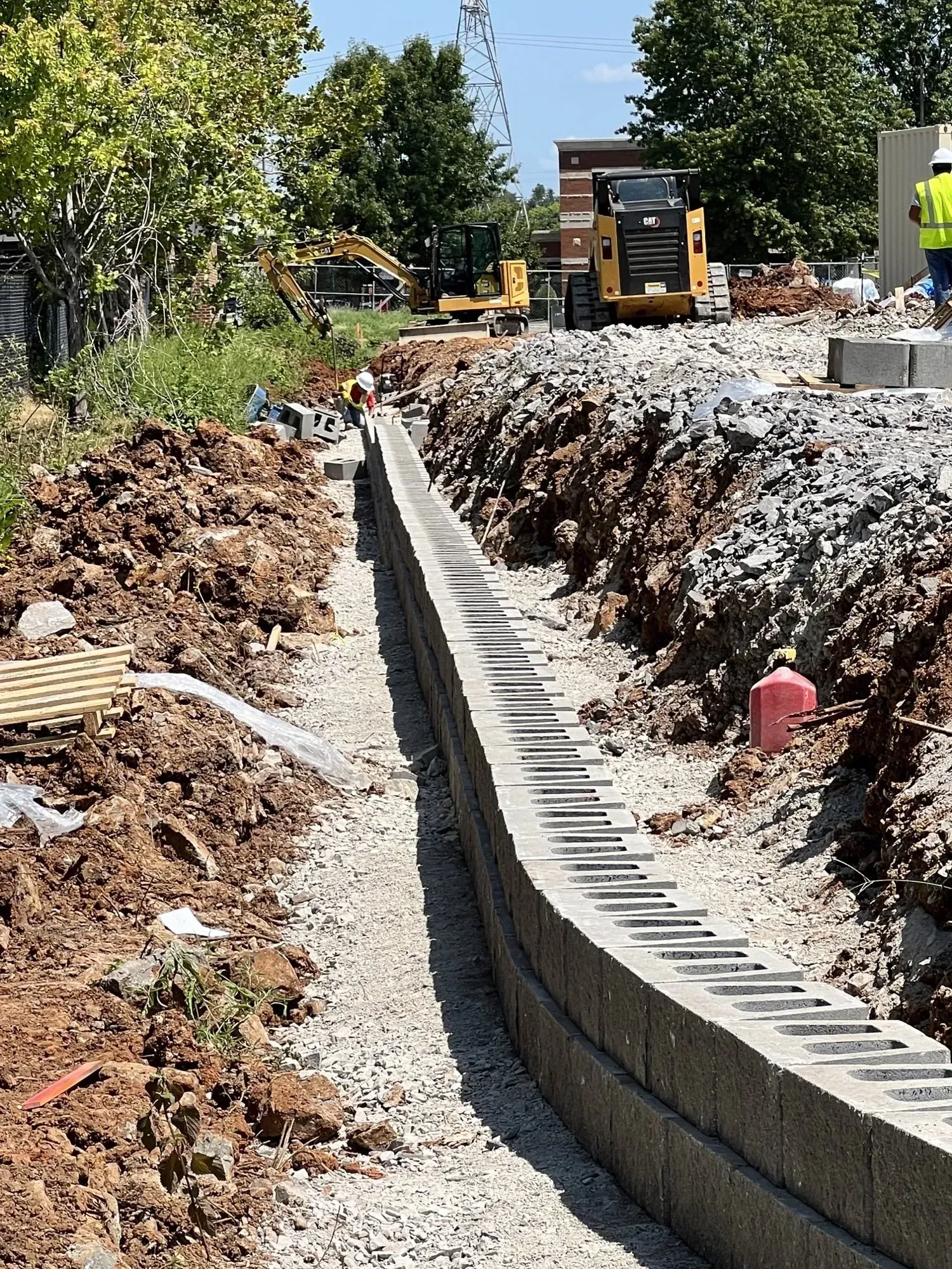 Construction of a retaining wall in a dirt trench. Yellow construction equipment is visible in the background.