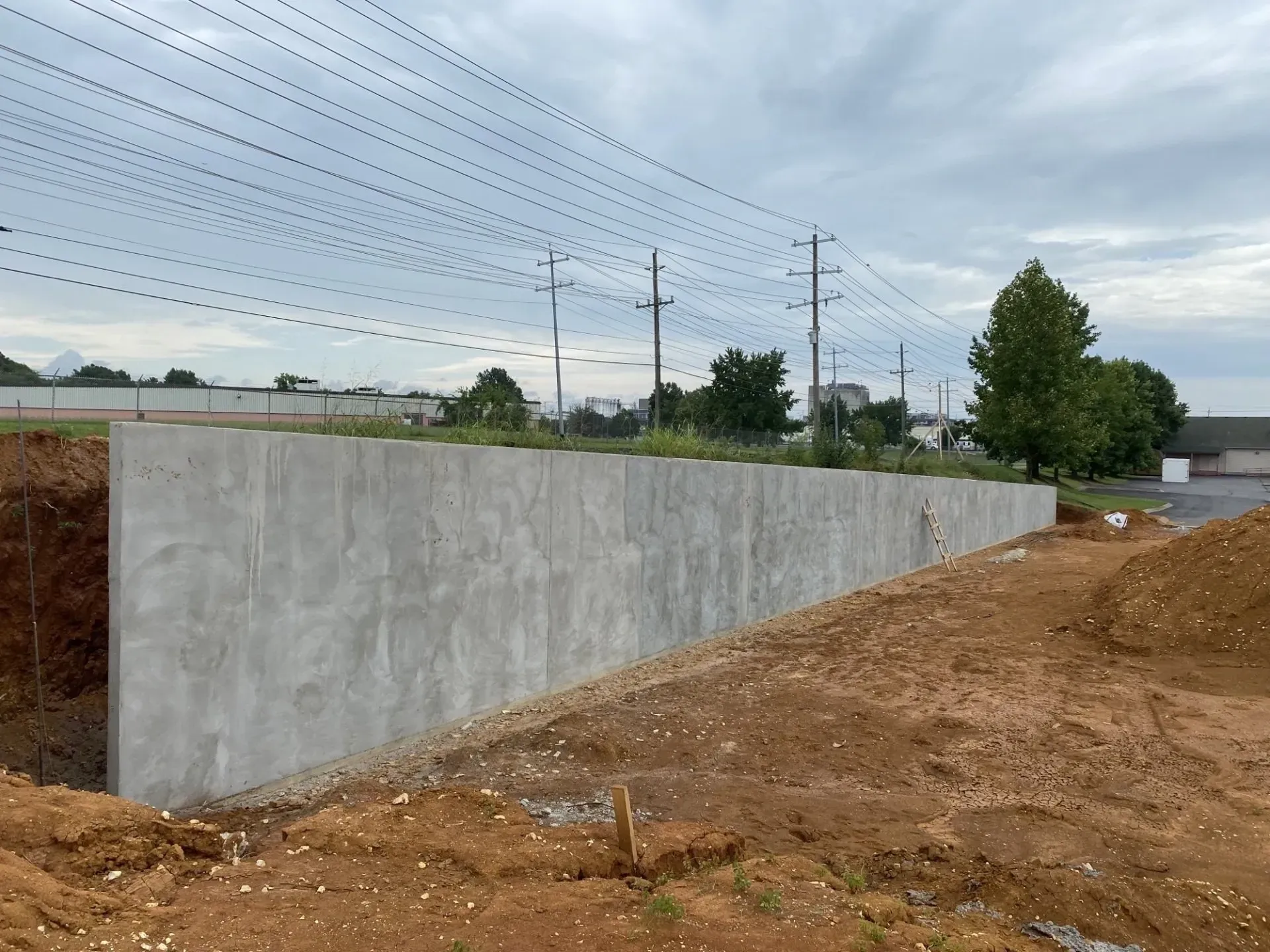Concrete retaining wall alongside a dirt construction site under a cloudy sky.