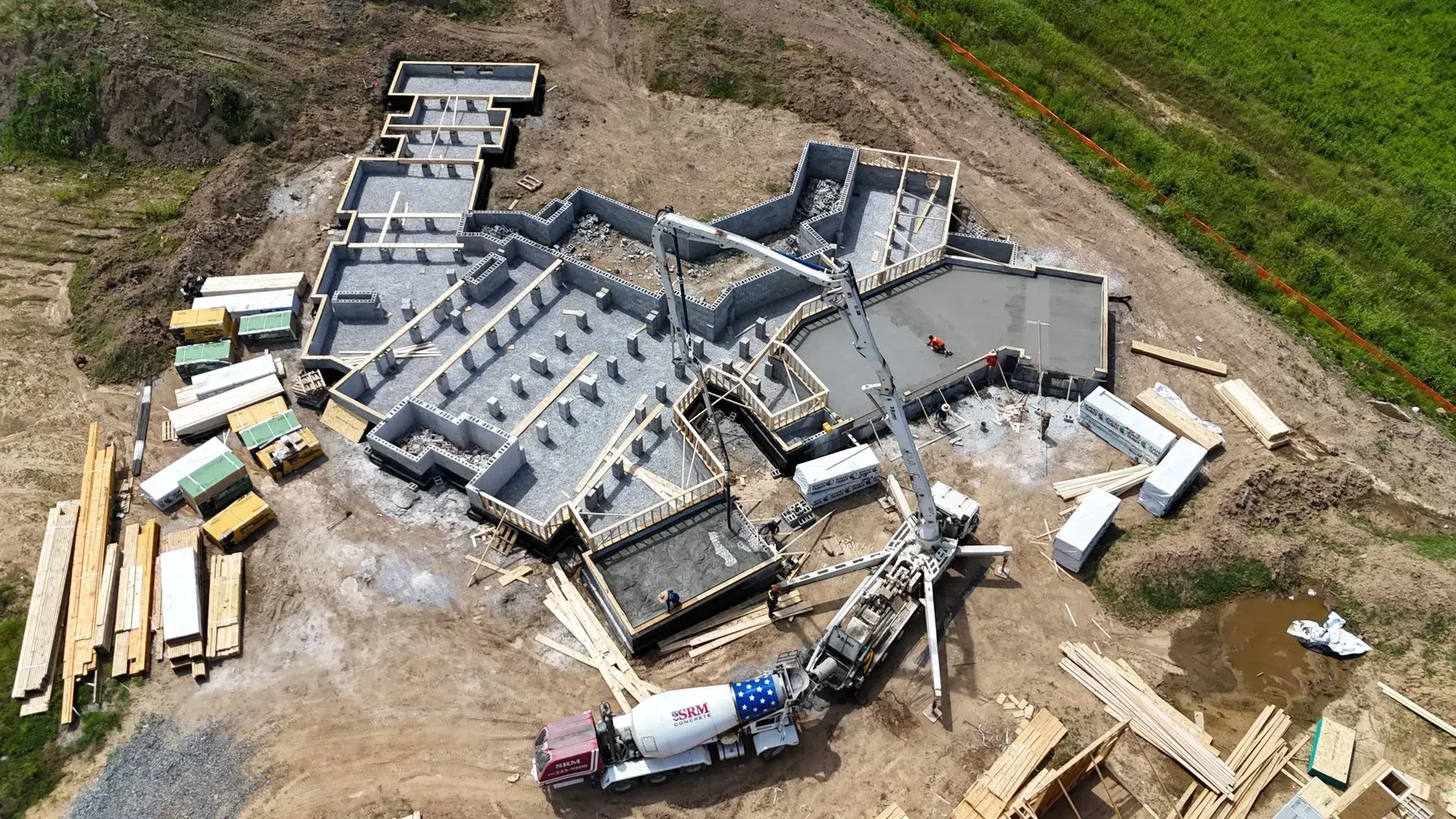 Aerial view of a building foundation being constructed, with a concrete mixer truck present on a dirt construction site.