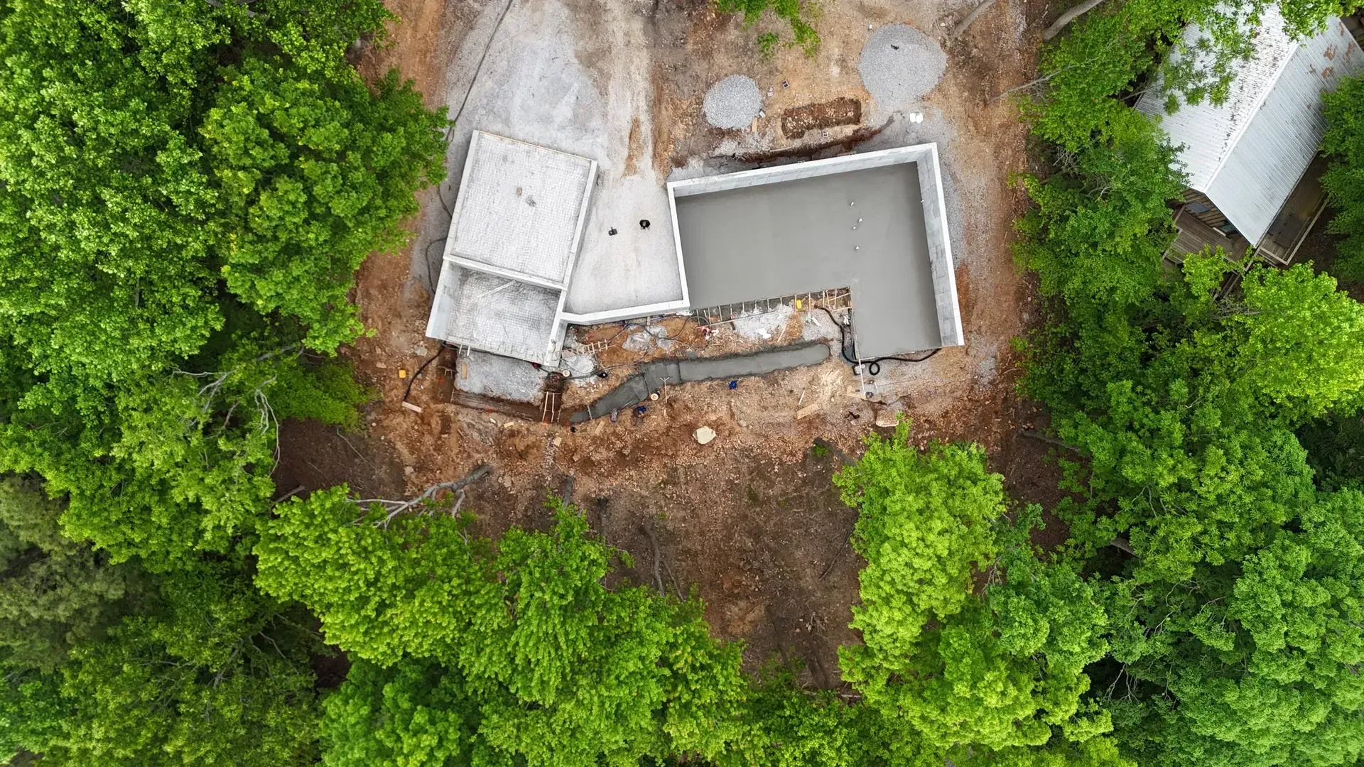 Aerial view of a concrete foundation for a building under construction, surrounded by trees and dirt.