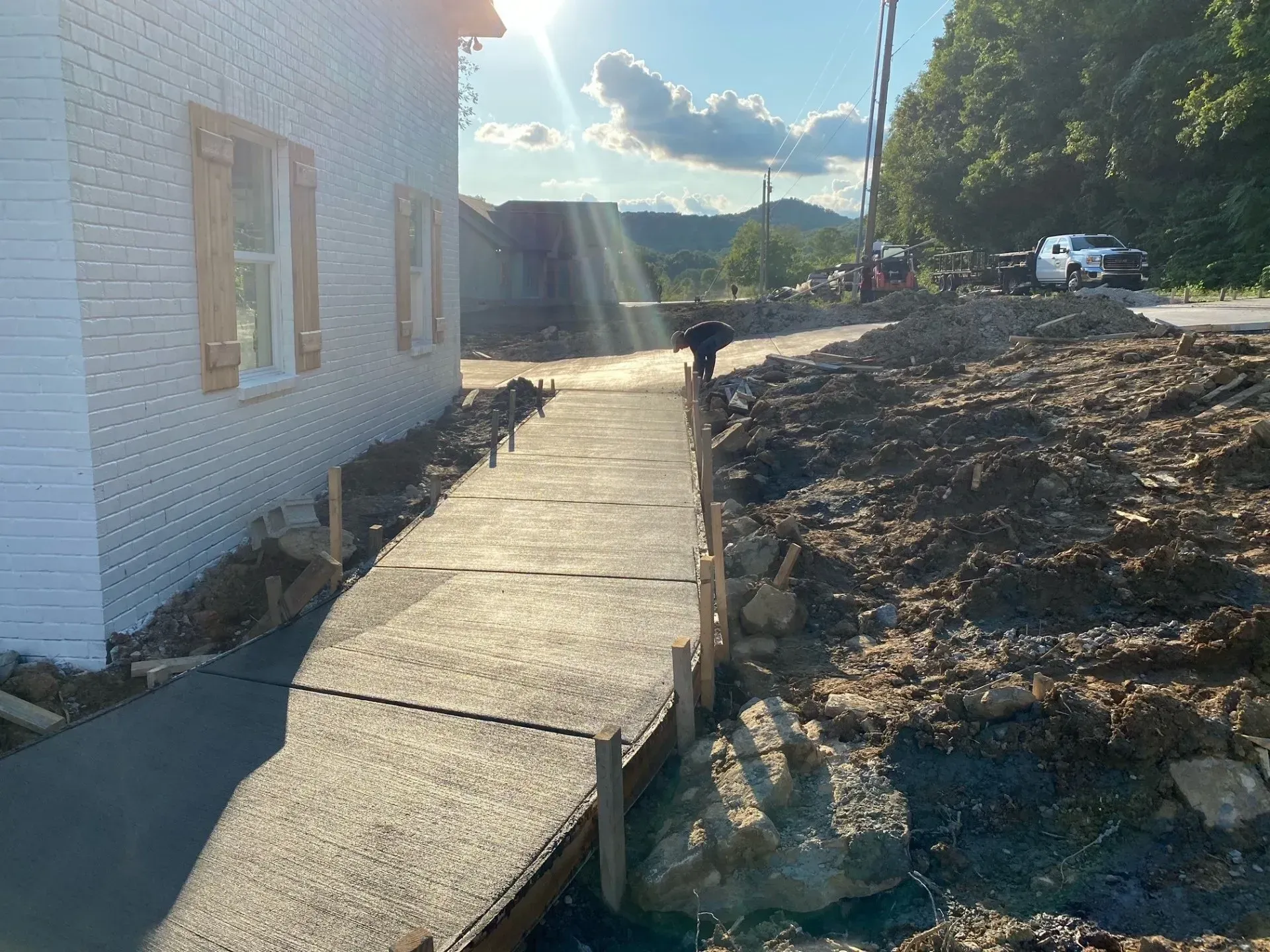New concrete walkway next to white building under construction, with sunny sky, dirt, and hills in background.