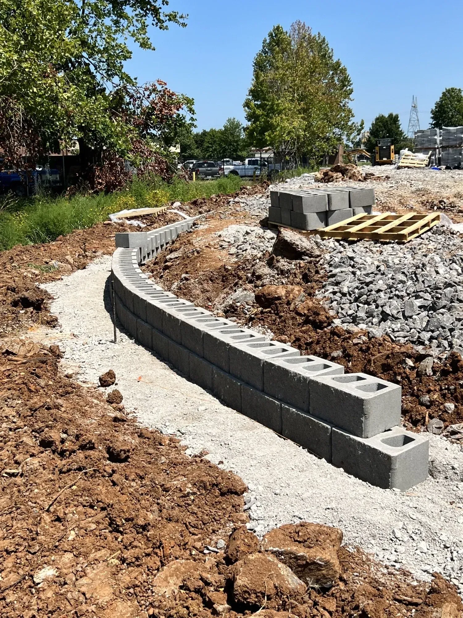Construction of a curved retaining wall using gray cinder blocks on a gravel base; outdoor setting.