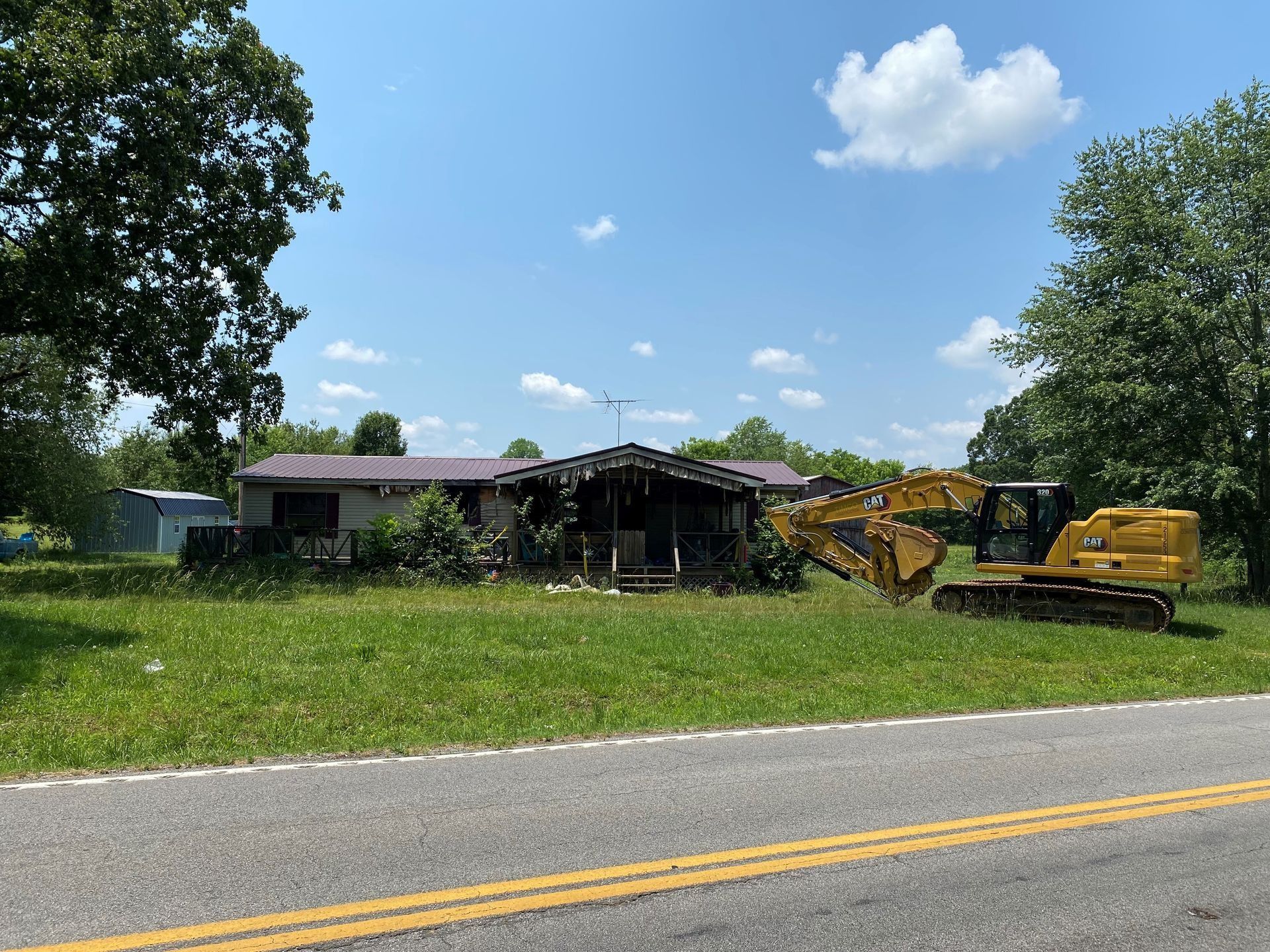 House being demolished by an excavator next to a road on a sunny day.